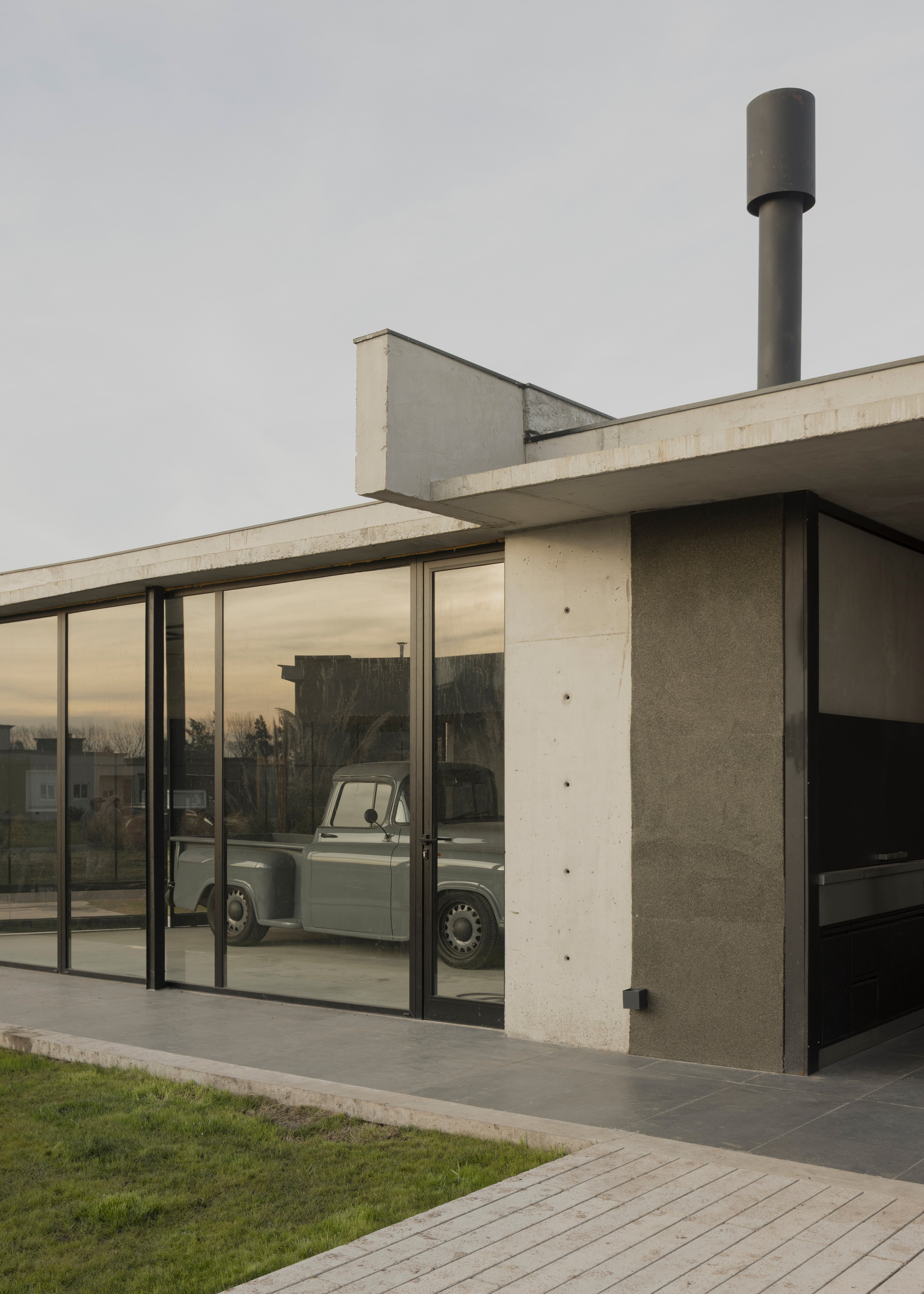 Exterior terrace with sliding glass walls reflecting a vintage truck and cylindrical chimney above