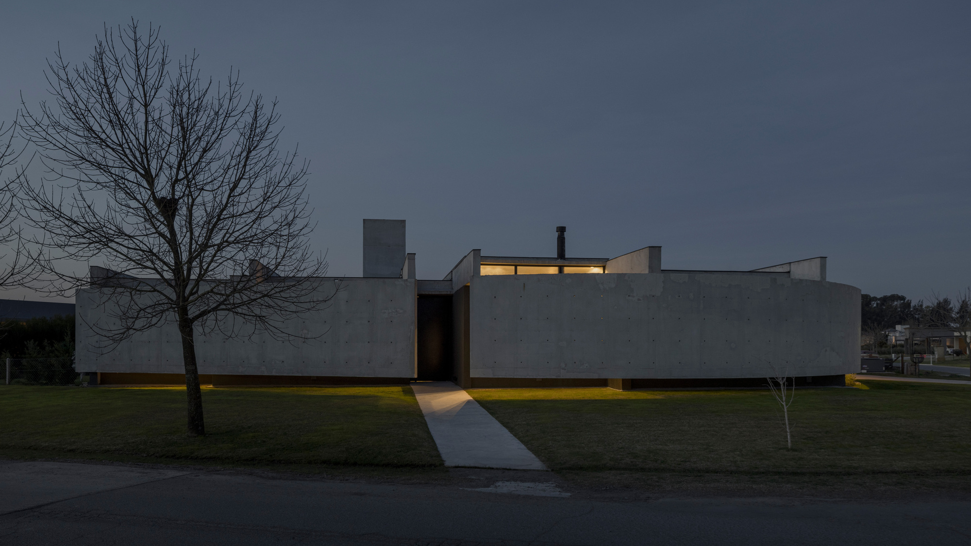 Front elevation at twilight with the recessed entry glowing beneath bare trees and dark sky