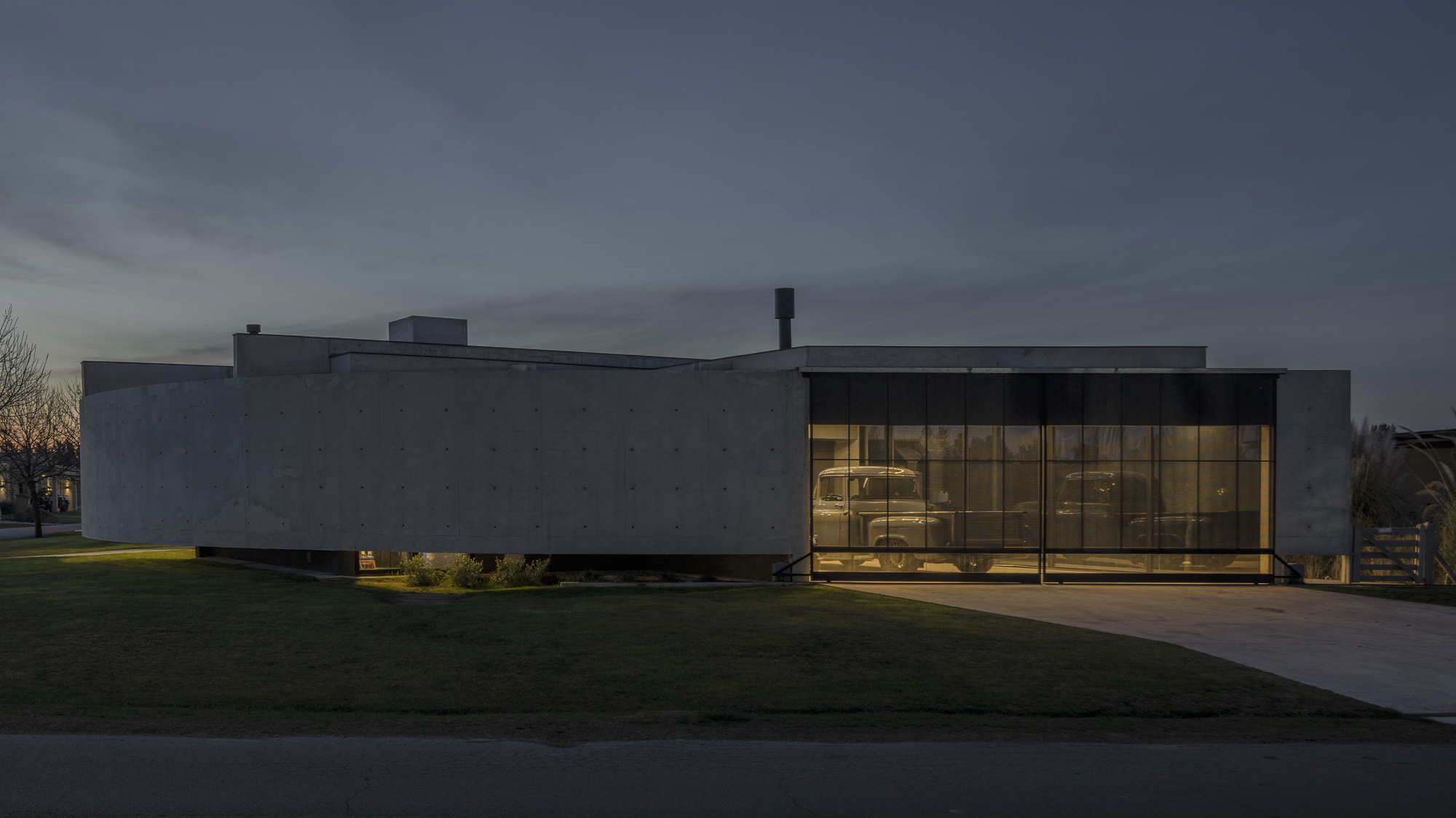 Twilight view of the glazed living pavilion with illuminated interiors visible through floor-to-ceiling windows