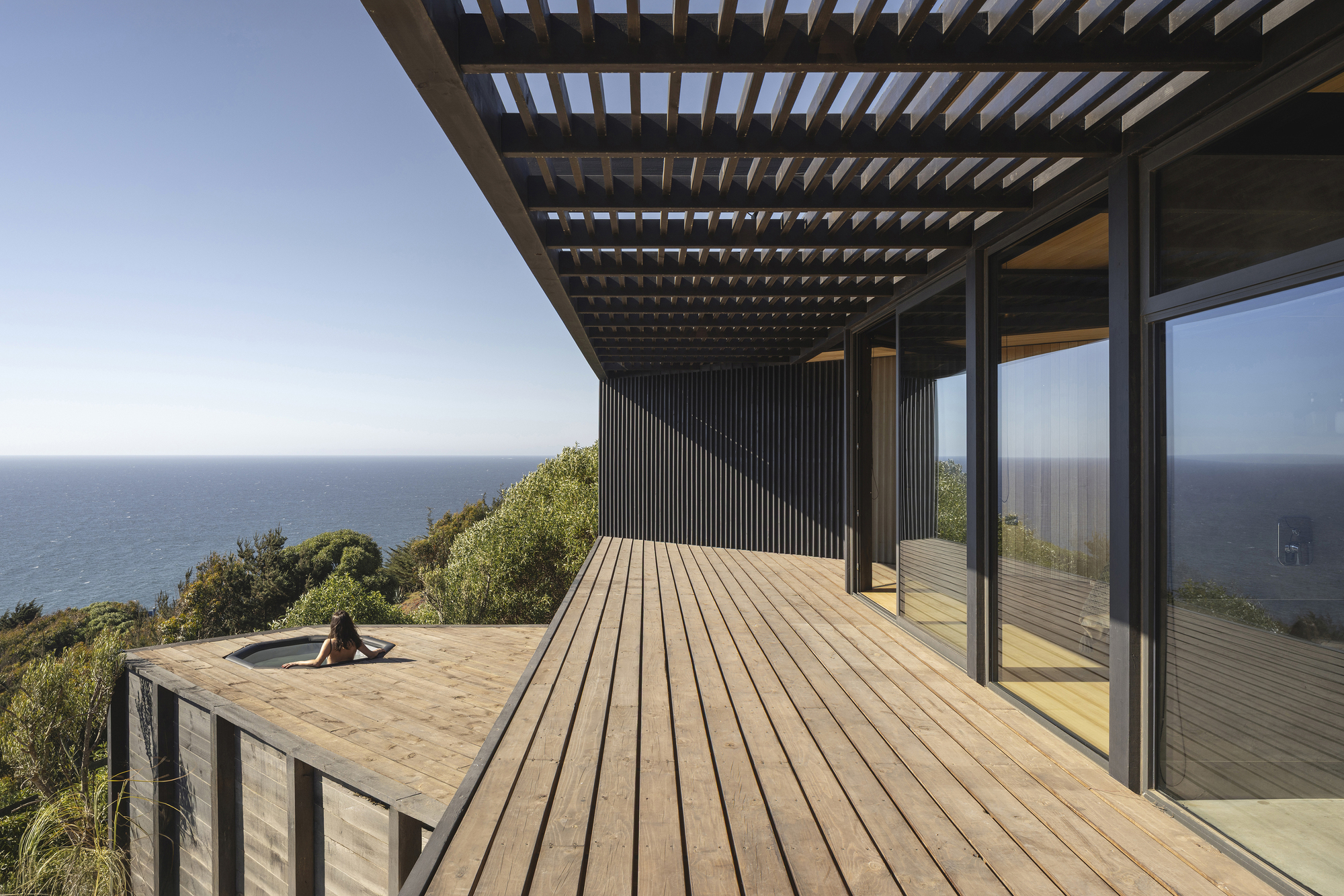 Timber deck with slatted pergola and corrugated wall panel overlooking ocean and native vegetation