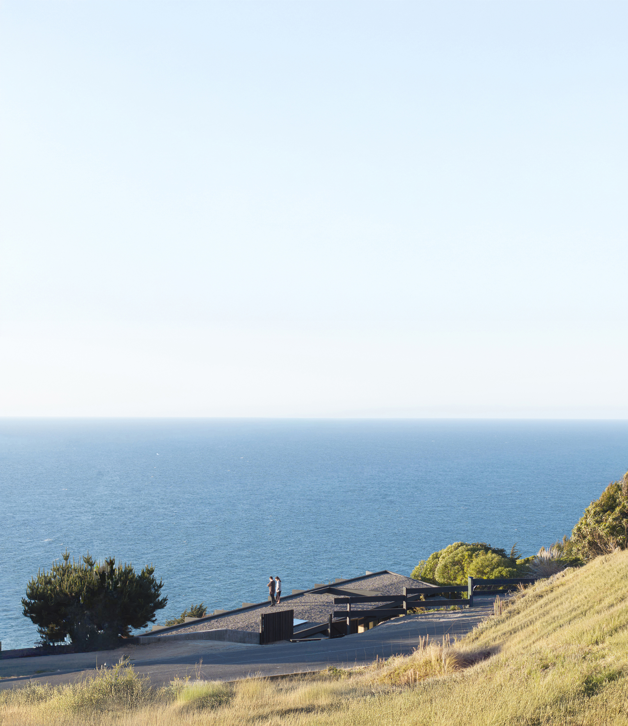 Distant view of the low-slung roof on coastal slope with two figures standing near the entrance