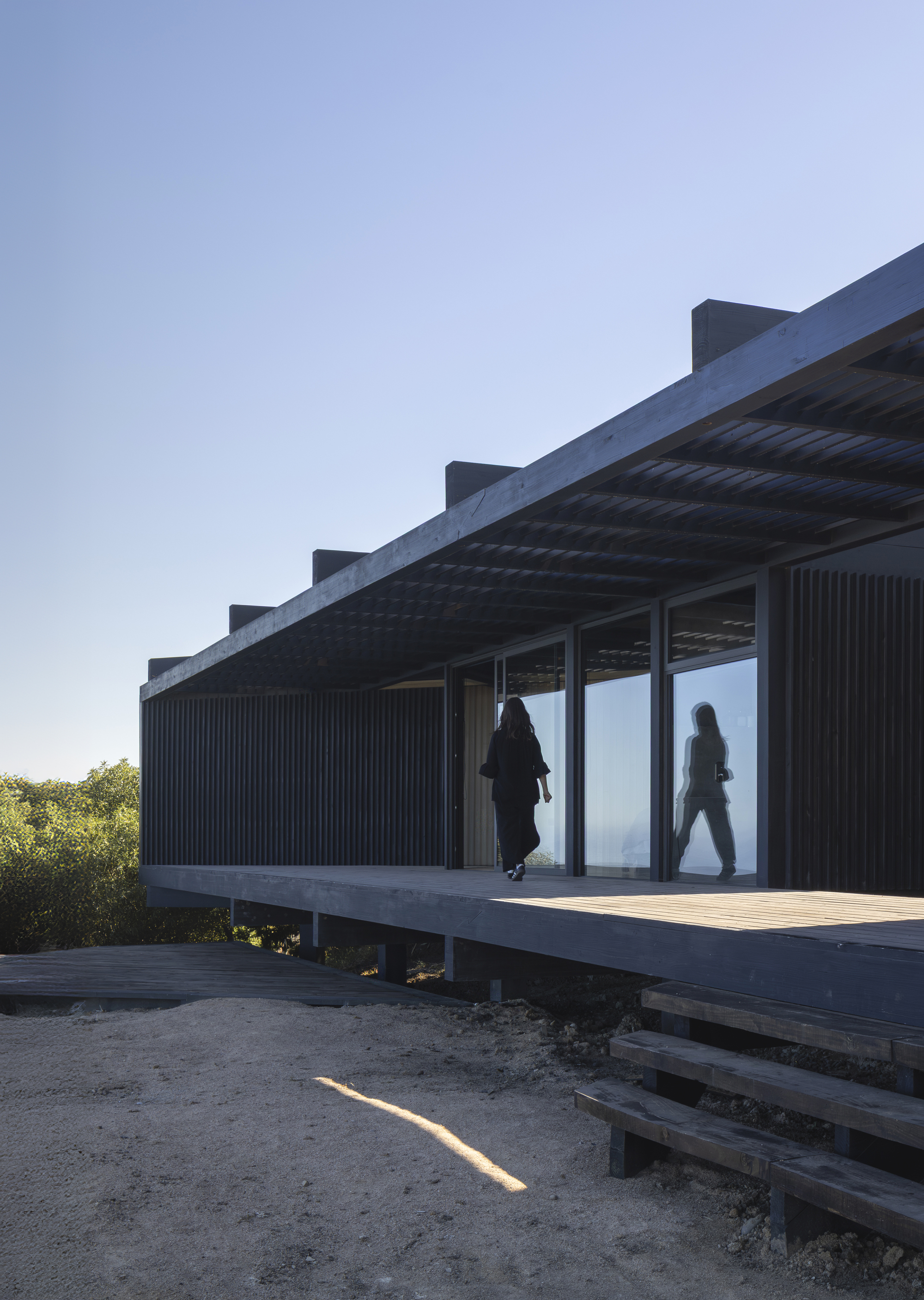 Elevated timber deck with corrugated metal cladding and residents passing through glass doors at dusk