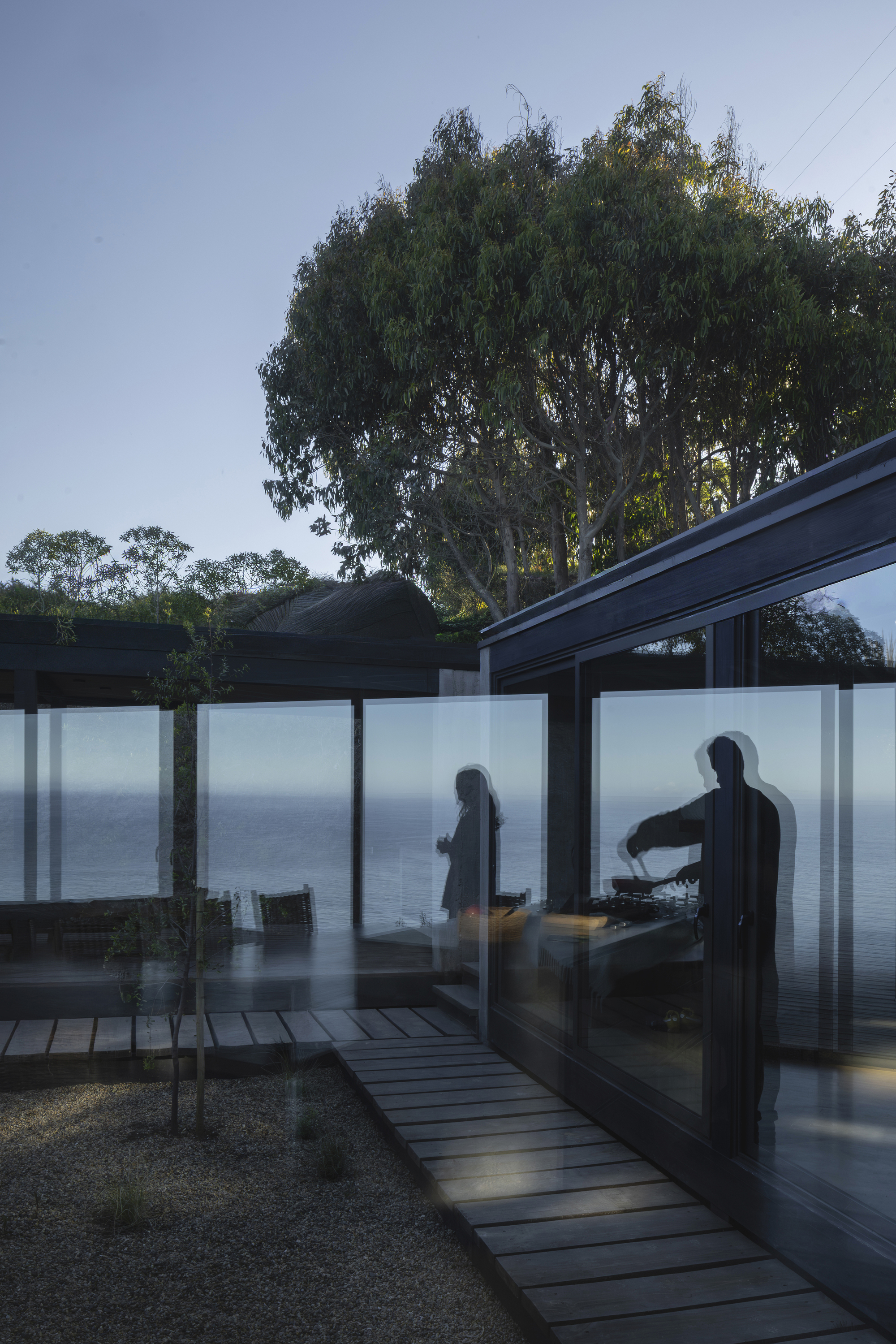 Frosted glass panels glowing at twilight with figures silhouetted against the ocean view