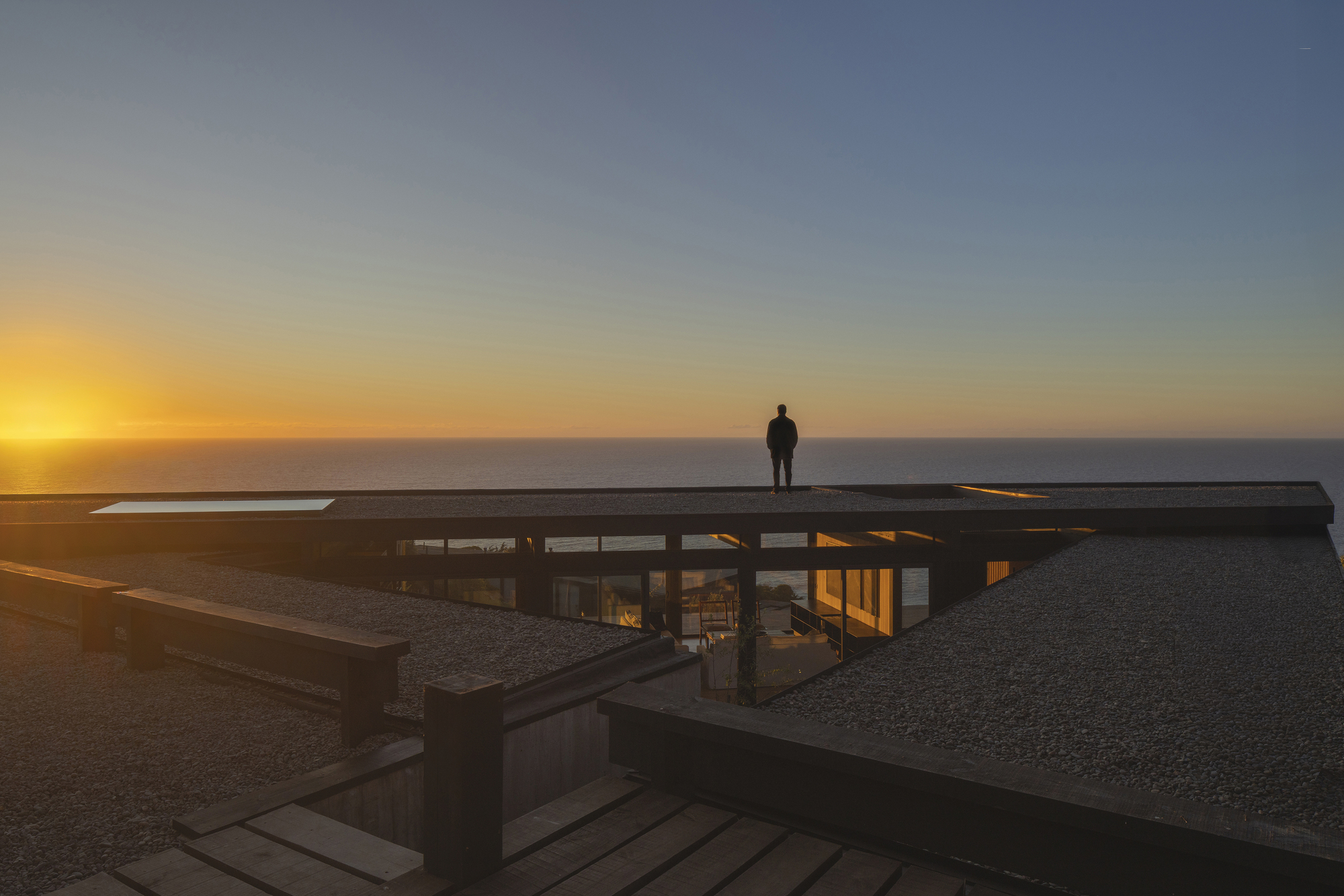 Flat roof with skylight and figure silhouetted against the ocean horizon at sunset