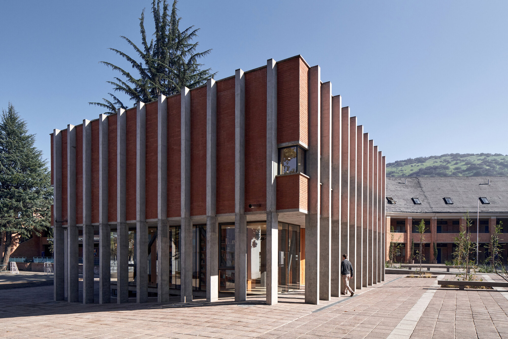 Pavilion with alternating red brick and white concrete fins on a paved plaza with surrounding trees