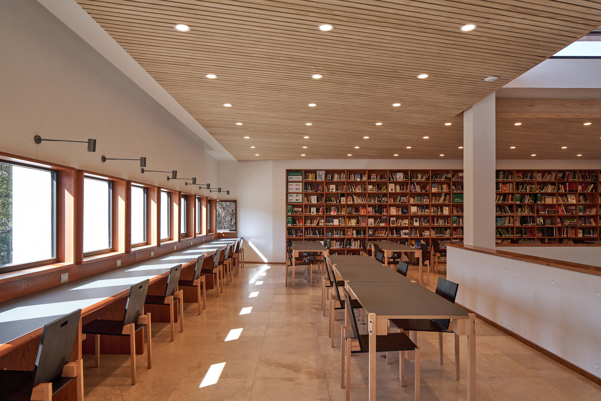 Reading room with timber slat ceiling, bookshelves along one wall and long study tables receiving daylight