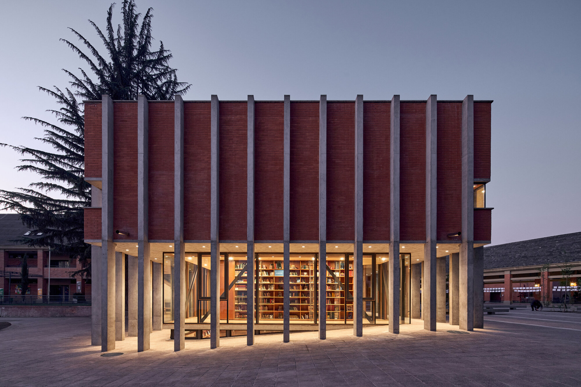 Front facade with illuminated interior visible between tall columns at dusk under a grey sky