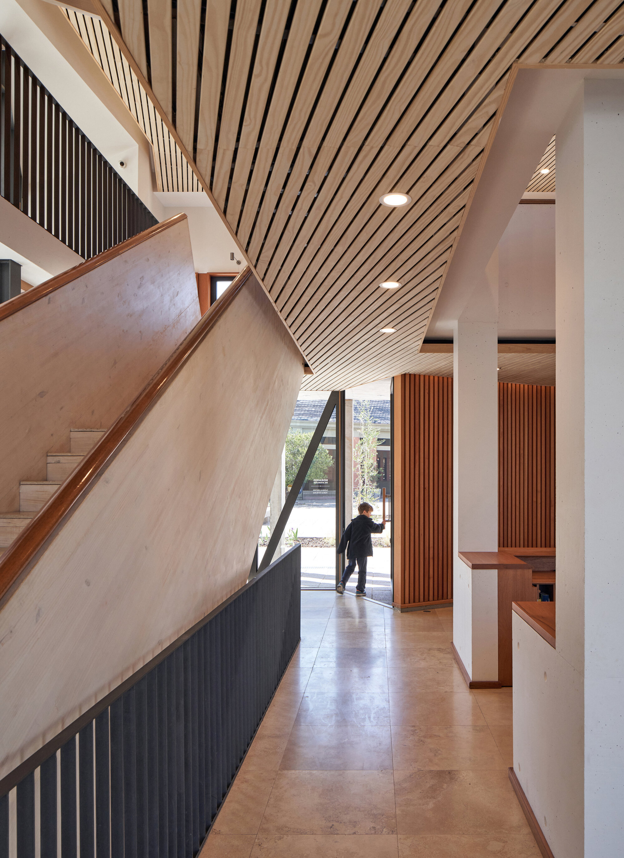 Entry hall with diagonal timber ceiling slats and a person approaching the glazed door