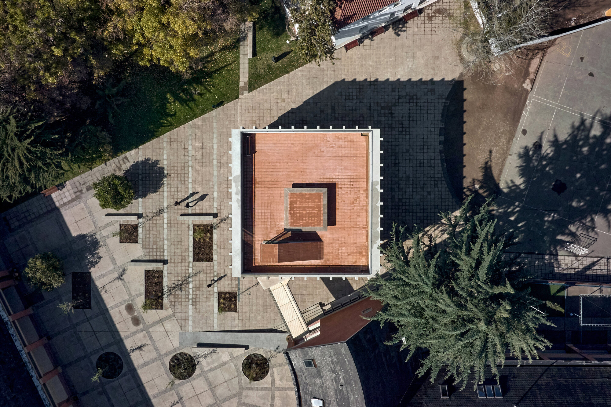 Aerial view of a courtyard with light and dark paving, circular planters and tree shadows