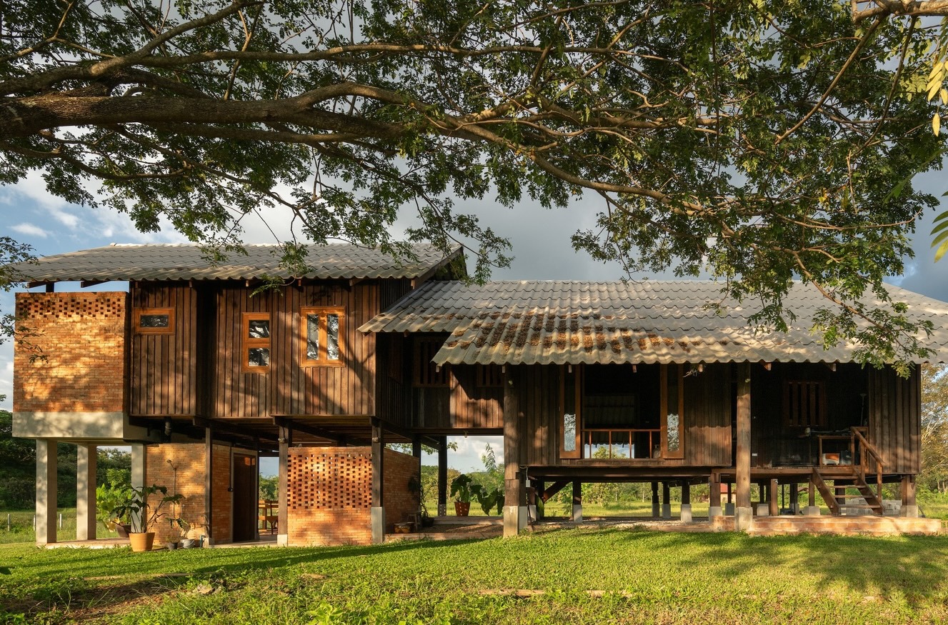 Elevated timber pavilions with corrugated metal roofing and perforated brick screens beneath overhanging tree branches