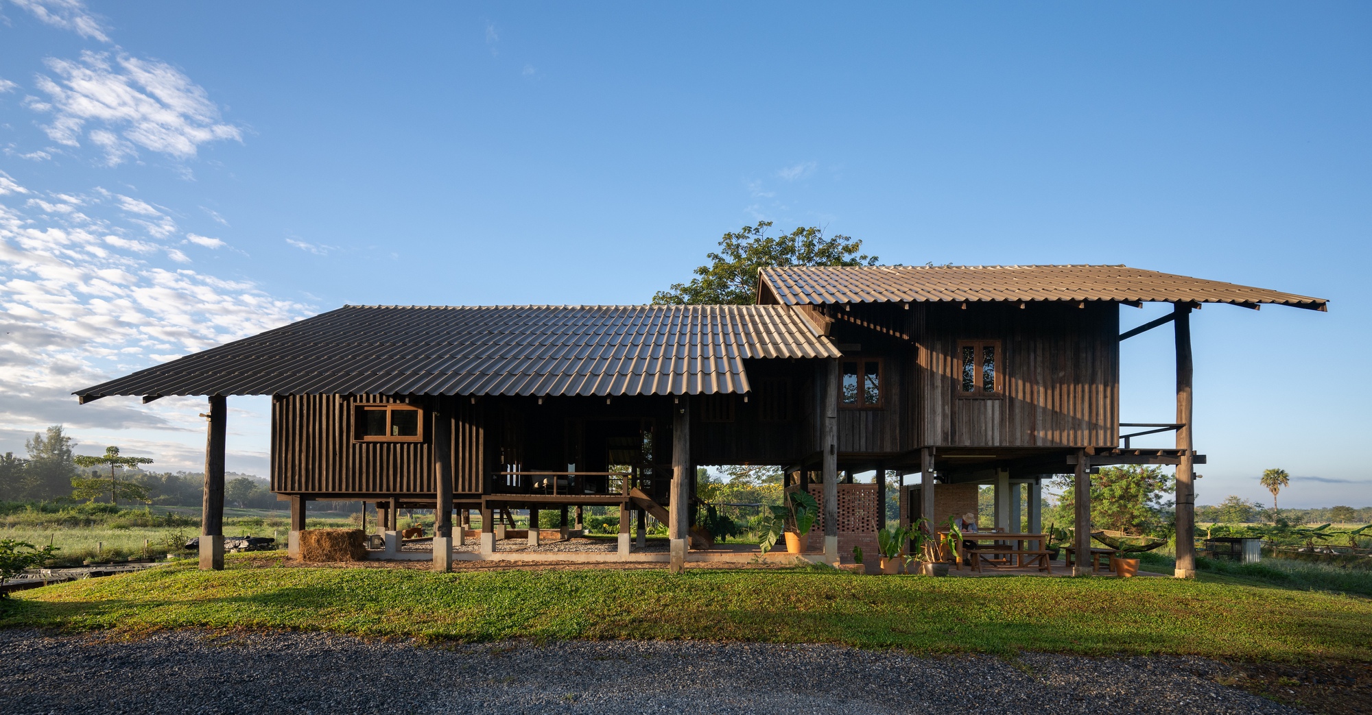 Elevated timber house on stilts with corrugated metal roofs under a blue sky with scattered clouds