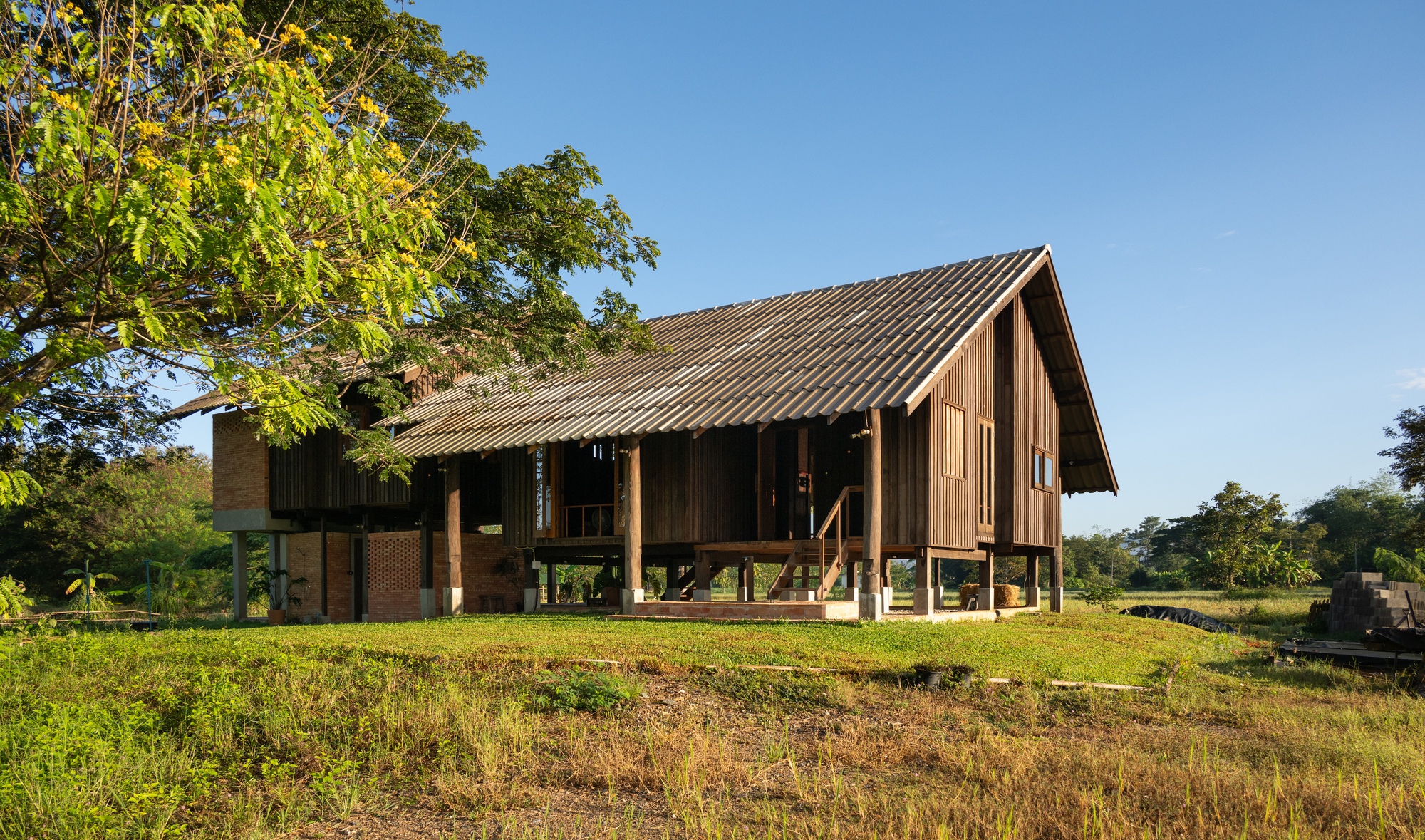 Gable end of the raised timber structure with overgrown grass foreground and distant hills