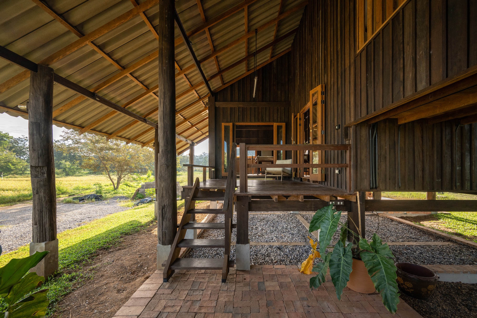 Covered ground level with wooden stair leading to elevated living space and gravel courtyard