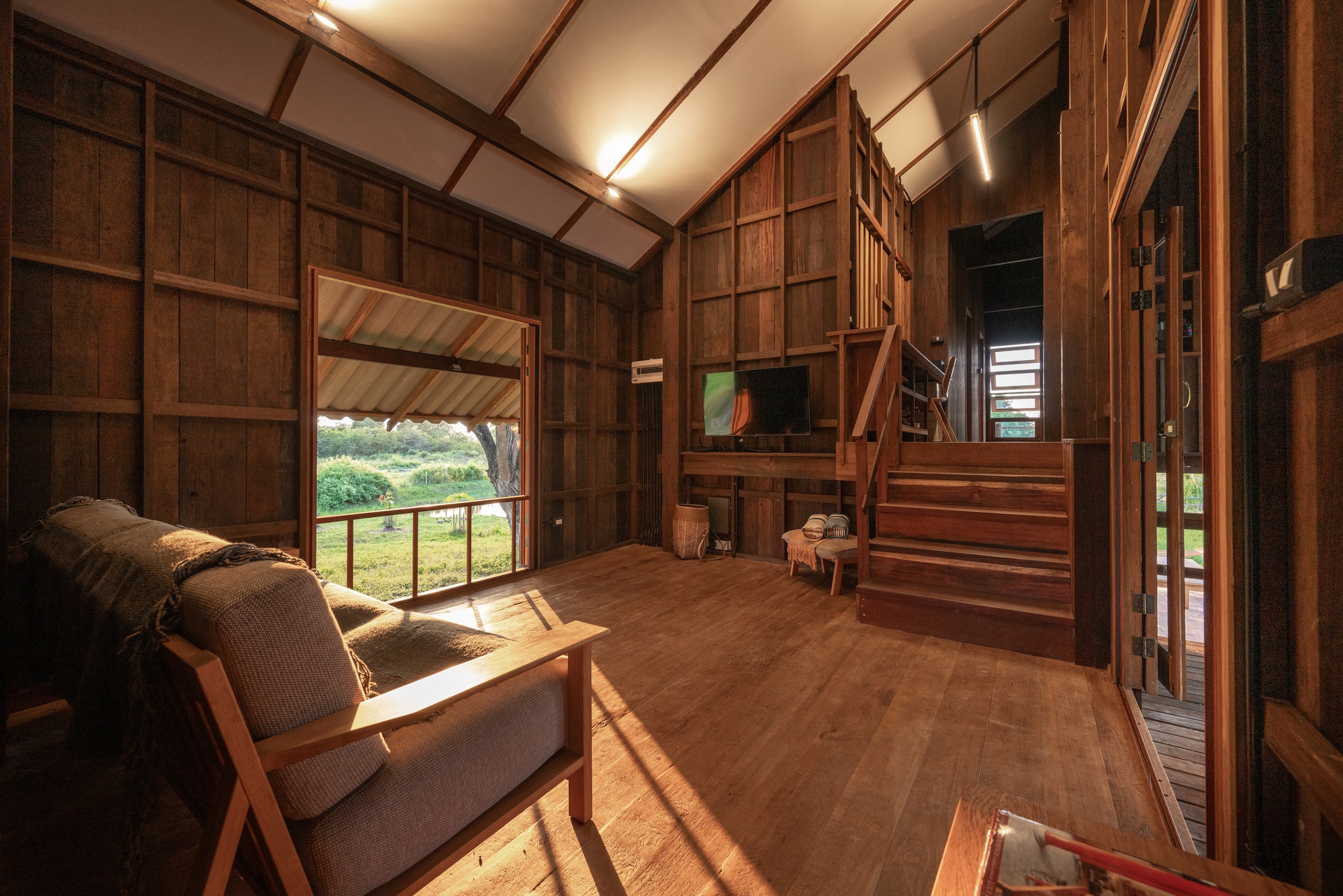 Interior living space with timber walls, exposed ceiling beams, and sunlight streaming through open doorway