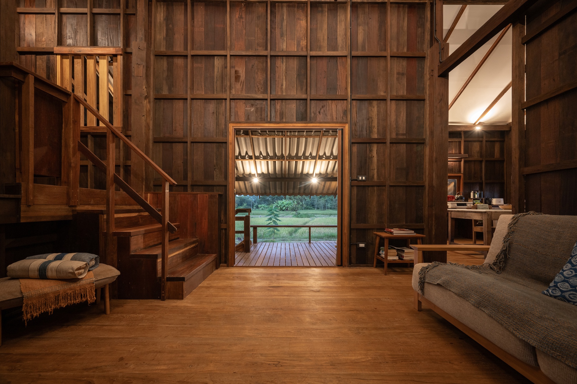 Timber-paneled interior with staircase and framed doorway opening to deck at dusk