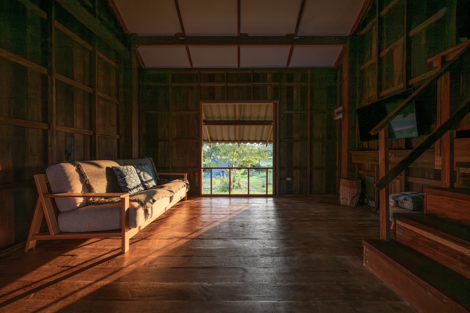 Living room with dark timber paneled walls and wooden flooring bathed in late afternoon sunlight