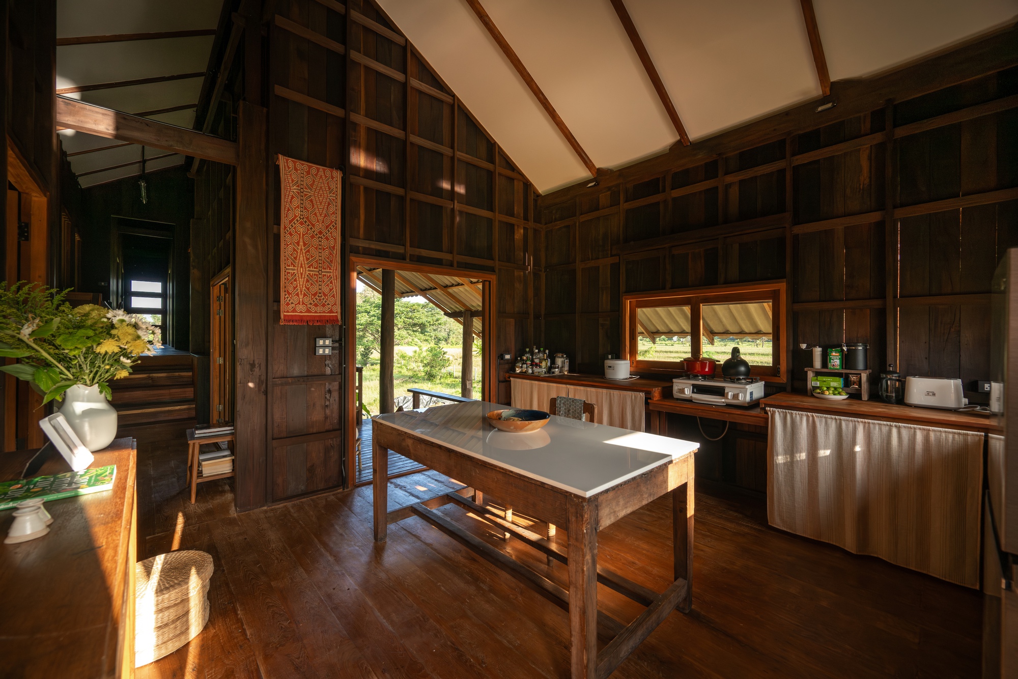 Open kitchen and dining area with timber cabinetry and a central work table beneath exposed rafters