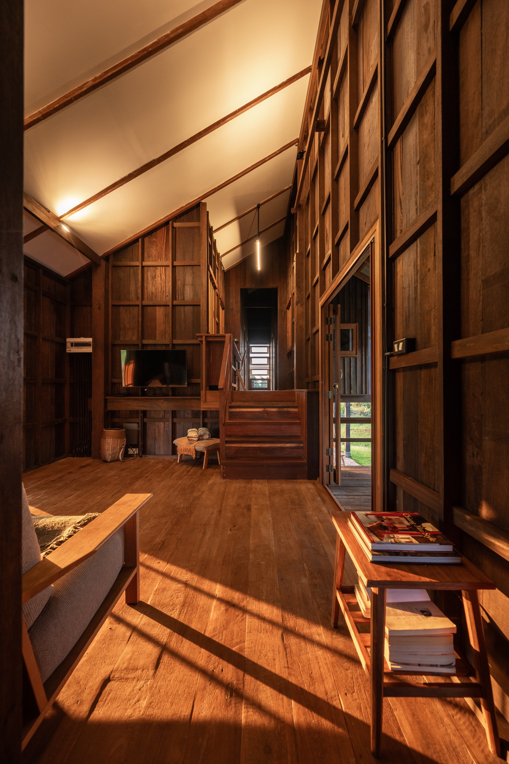 Double-height interior volume with timber staircase and wall paneling catching diagonal sunlight patterns