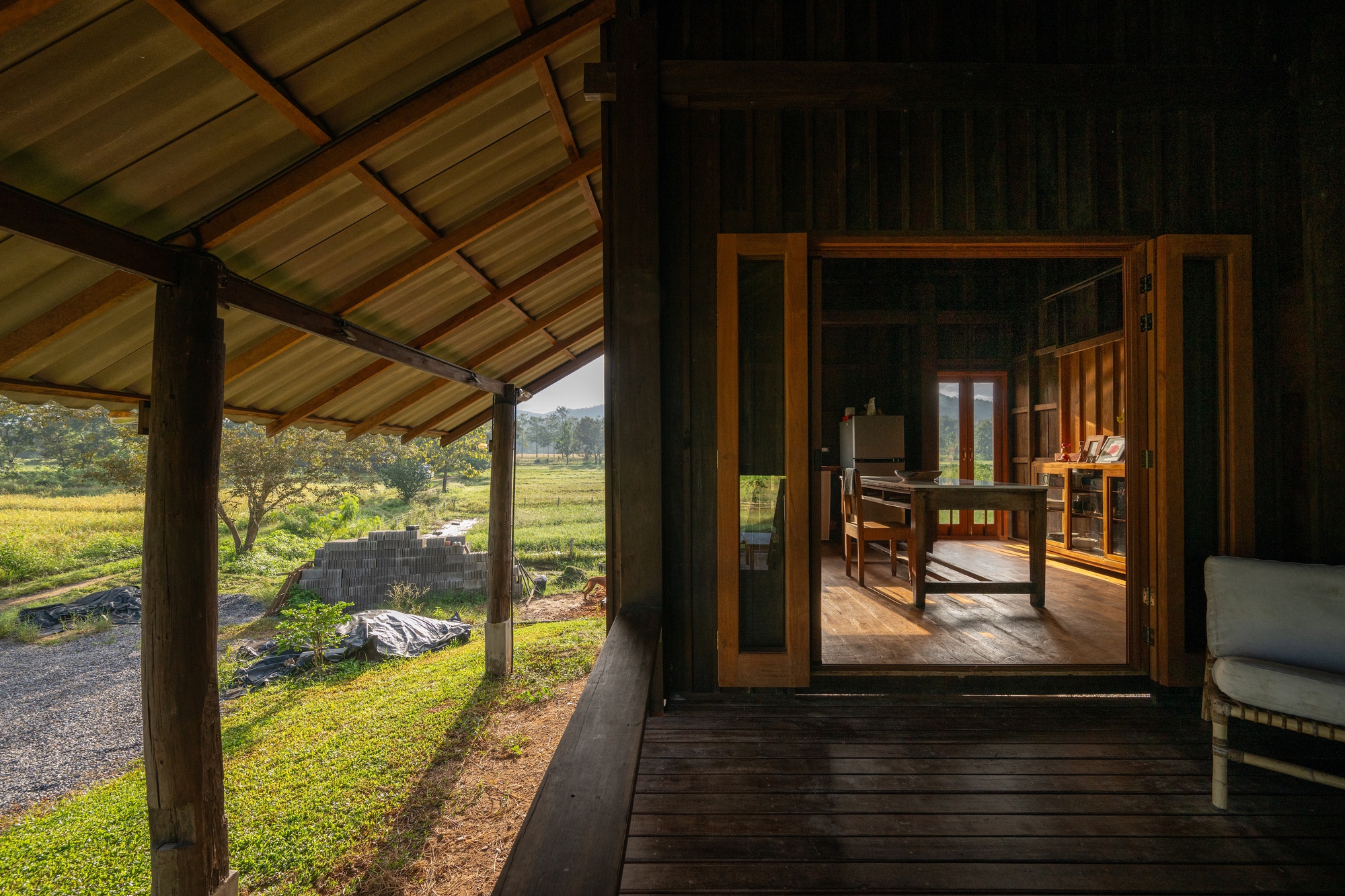 Covered timber deck looking through glass doors into the interior with rice fields beyond