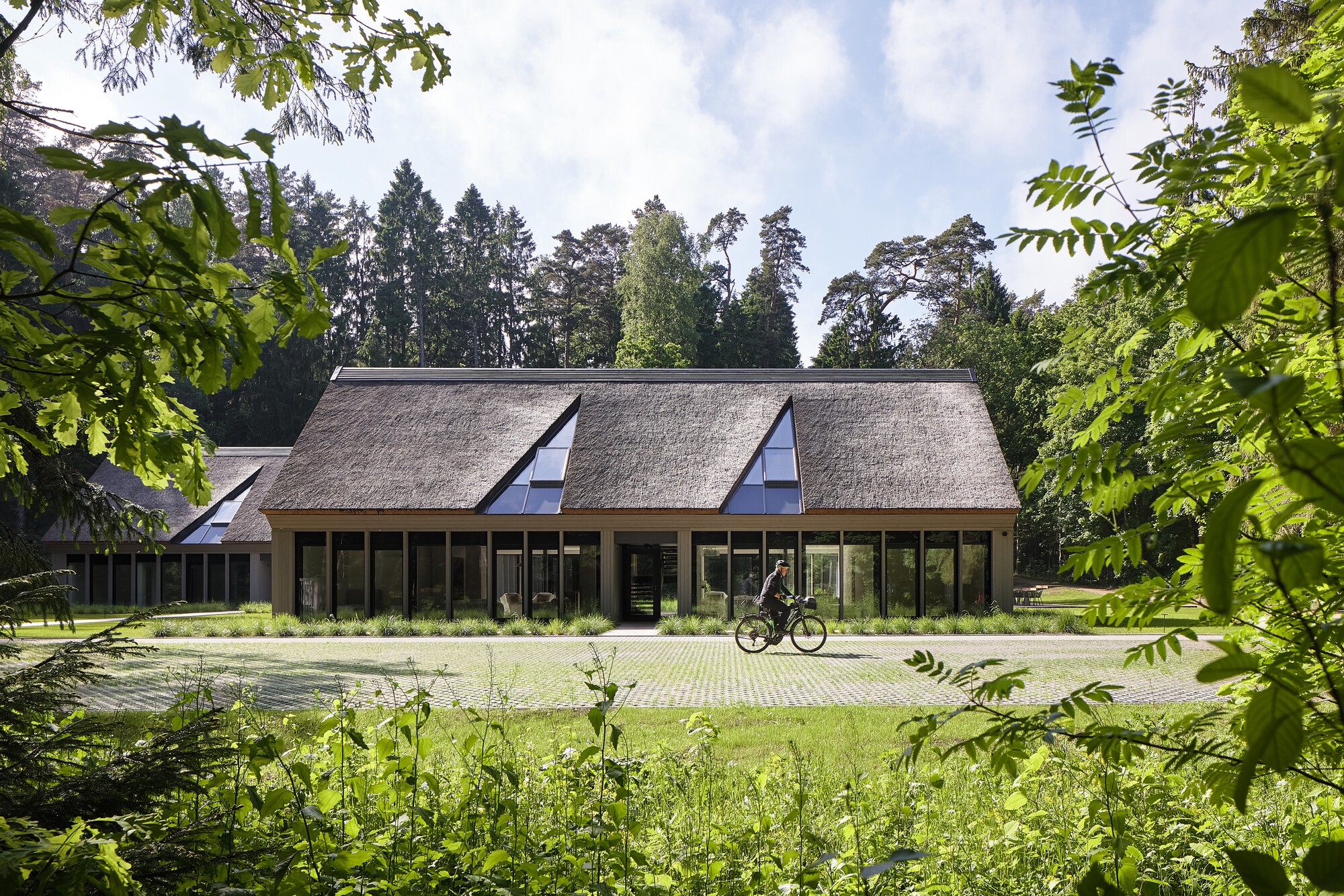 Thatched roof facade with triangular dormer windows and full-height glazing as a cyclist passes