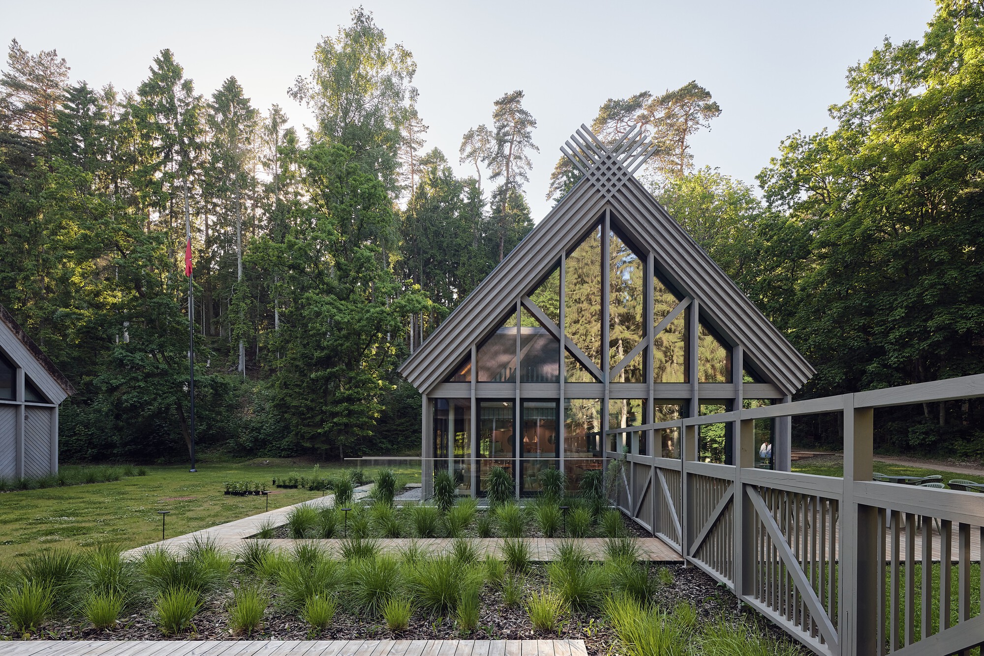 Glazed gable end with exposed timber bracing and diagonal roof cladding at dusk