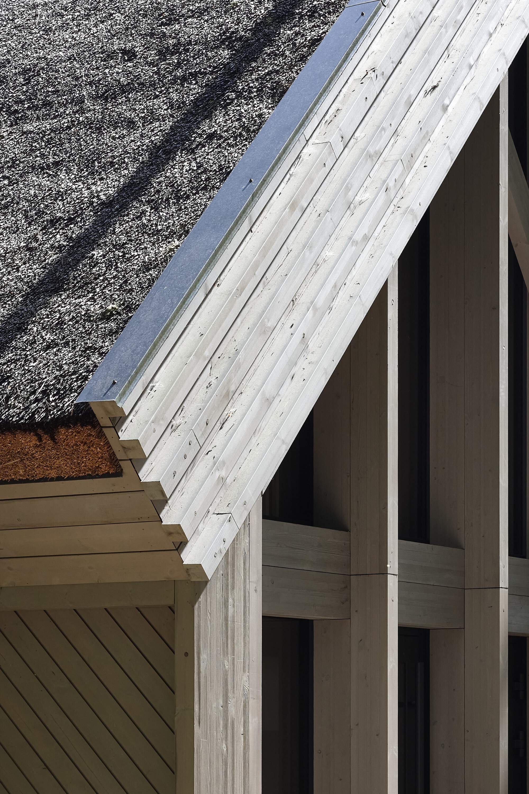 Detail of weathered timber rafter meeting vertical columns against gravel courtyard
