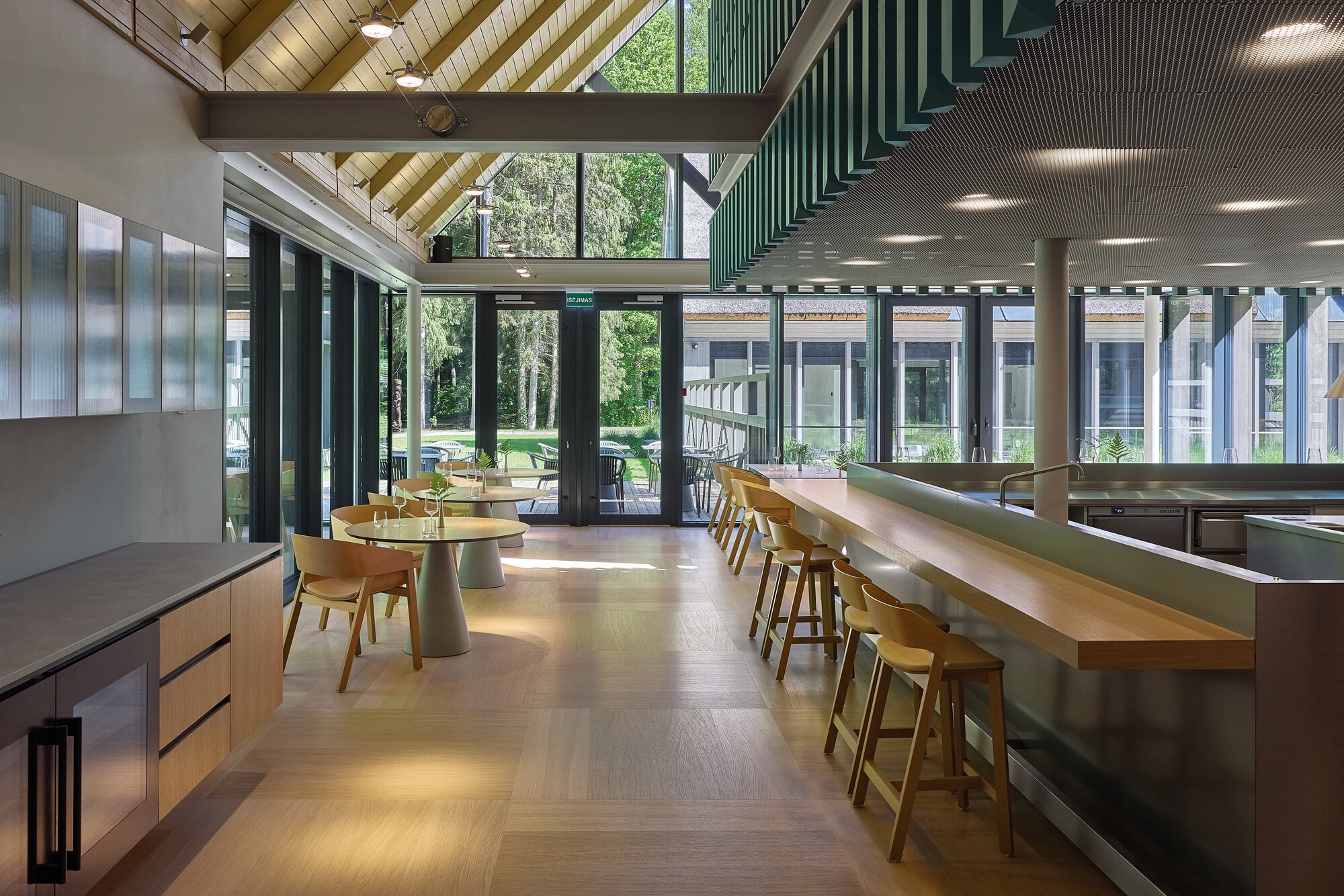View through the dining space toward glazed doors opening onto a lawn with trees beyond