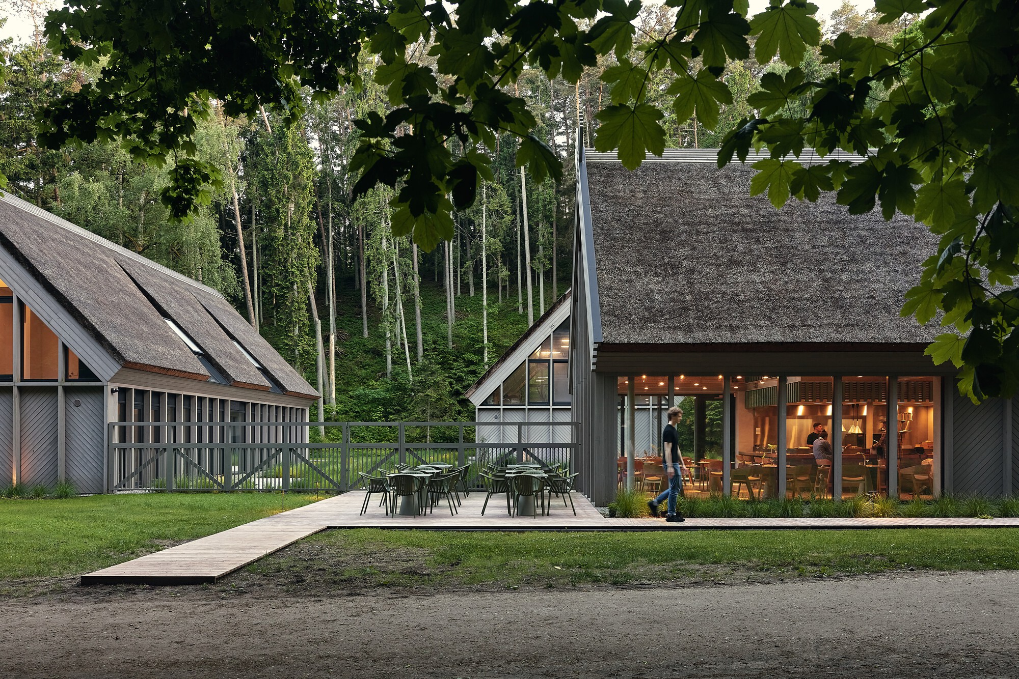 Evening view of thatched-roof pavilions with outdoor seating terrace and a person walking across the lawn