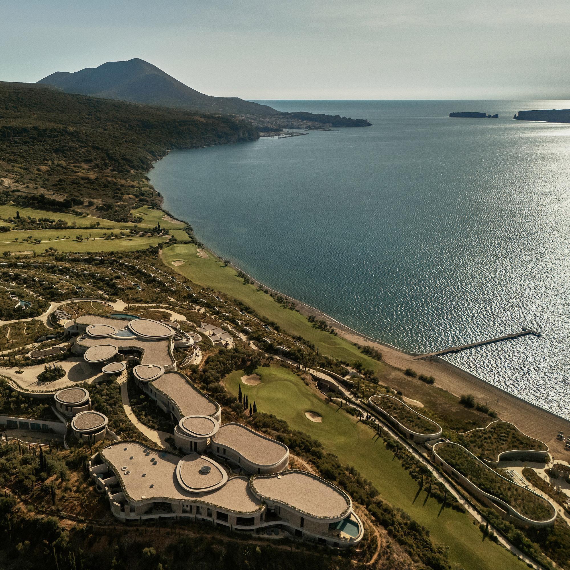 Aerial view of clustered circular roof forms along a coastal bay with golf course and mountains