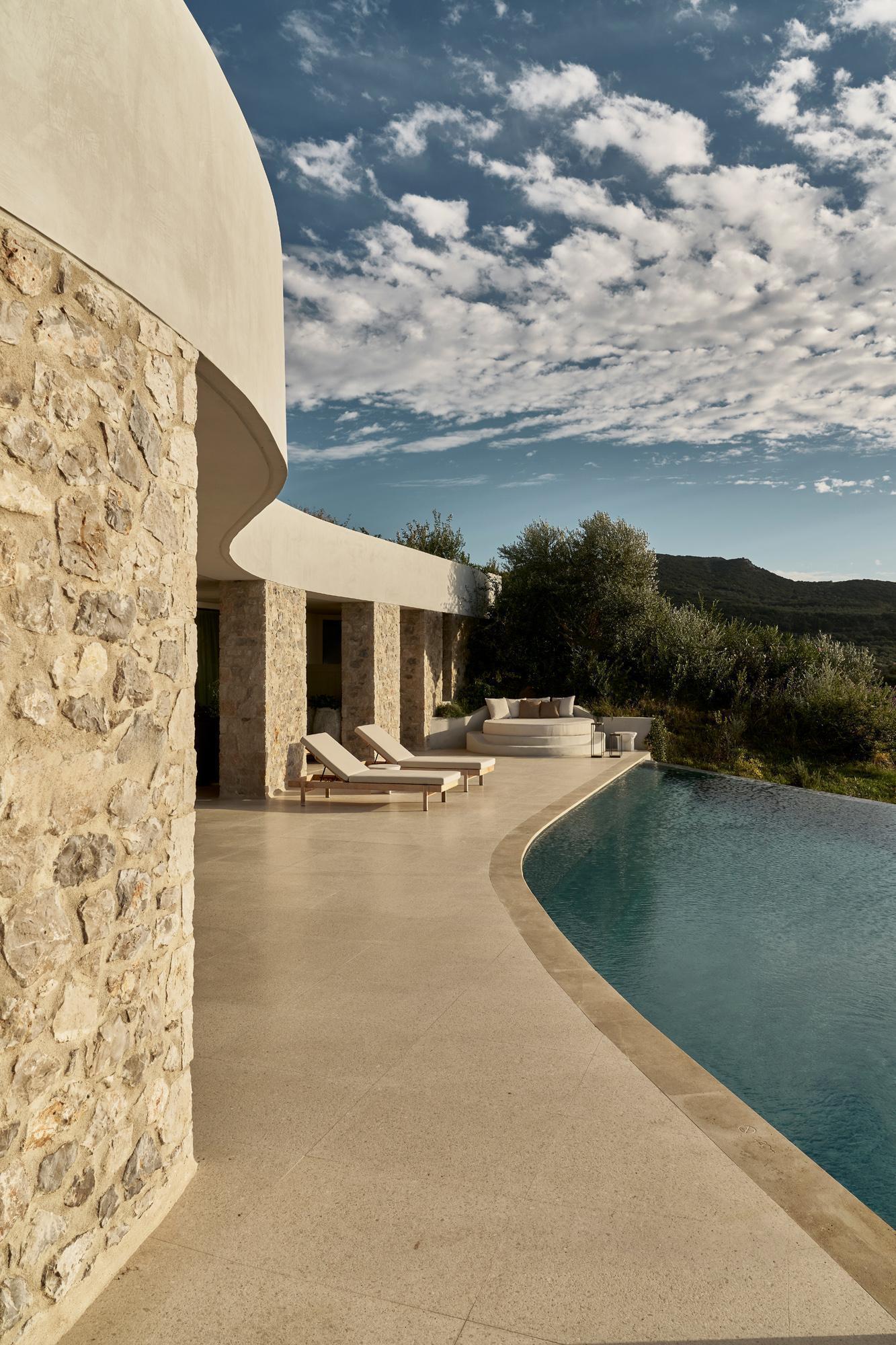 Poolside terrace with stone walls and curving white canopy overlooking hillside under bright sky