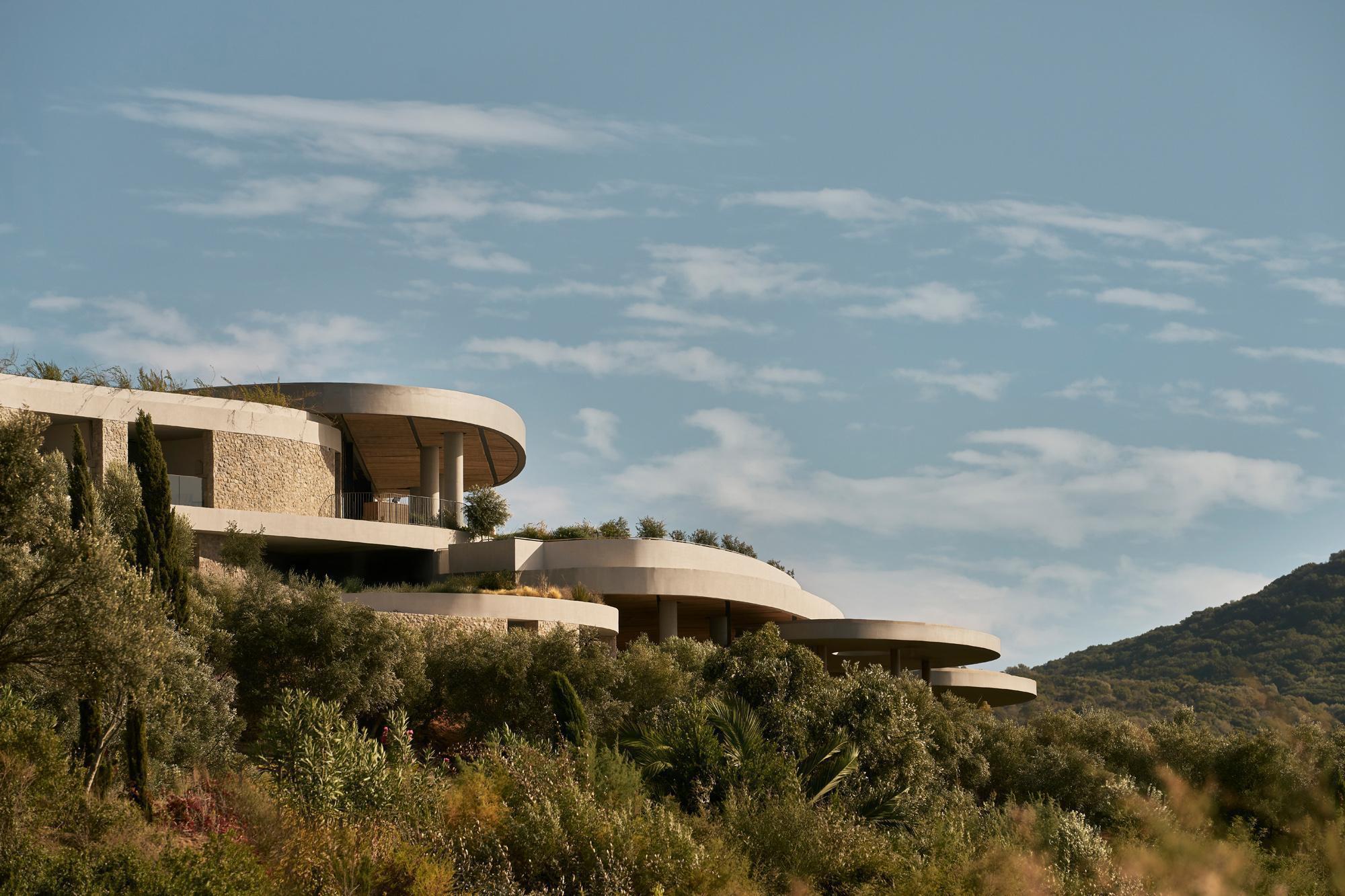 Layered circular terraces stepping down a hillside planted with olive trees and native desert vegetation