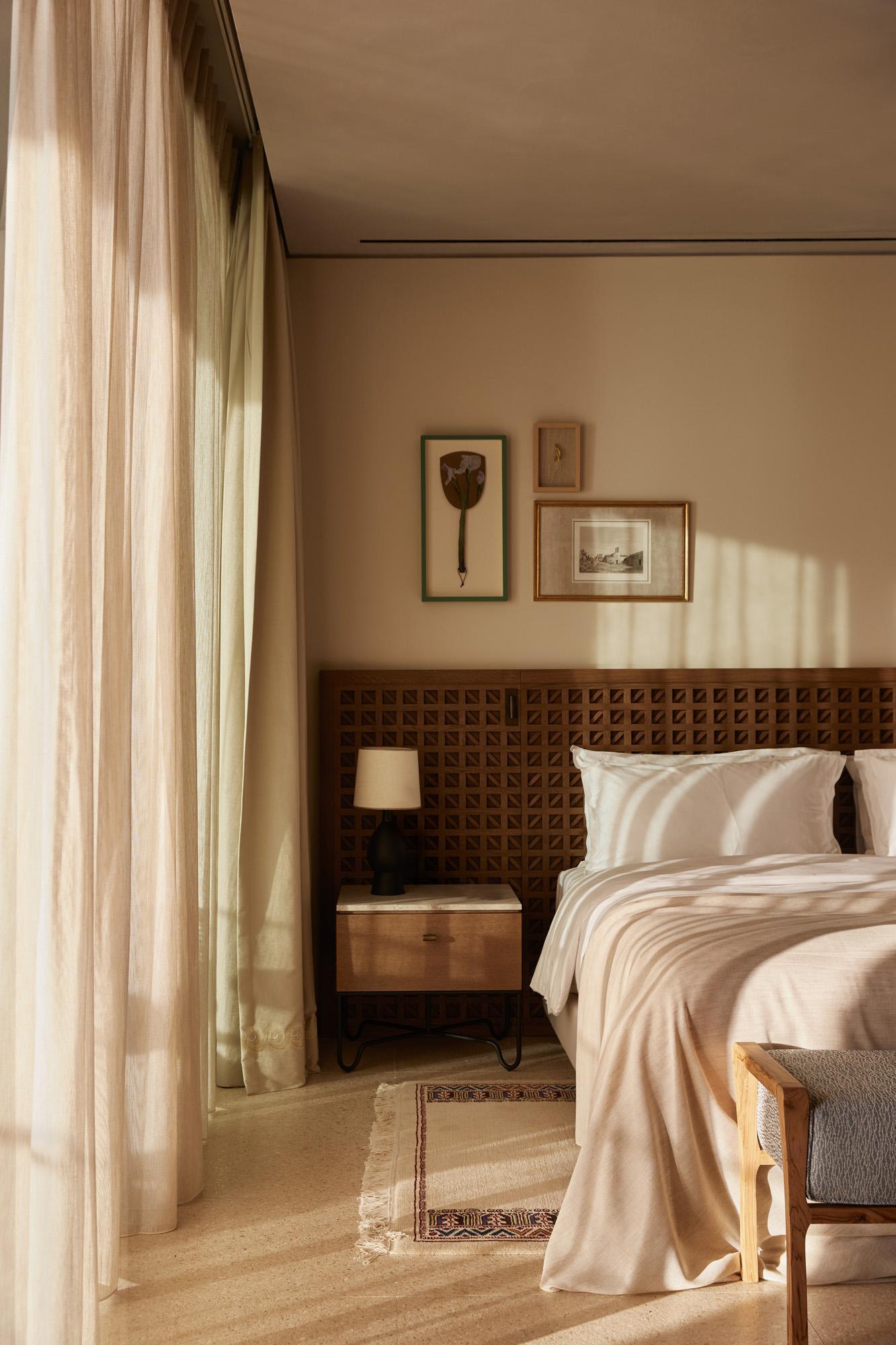 Bedroom interior with carved wood headboard and sheer curtains filtering warm afternoon light