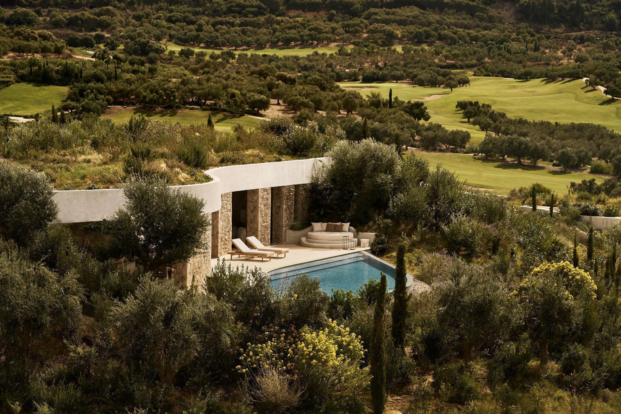 Stone pavilion and pool terrace overlooking a golf course landscape with cypress and olive trees