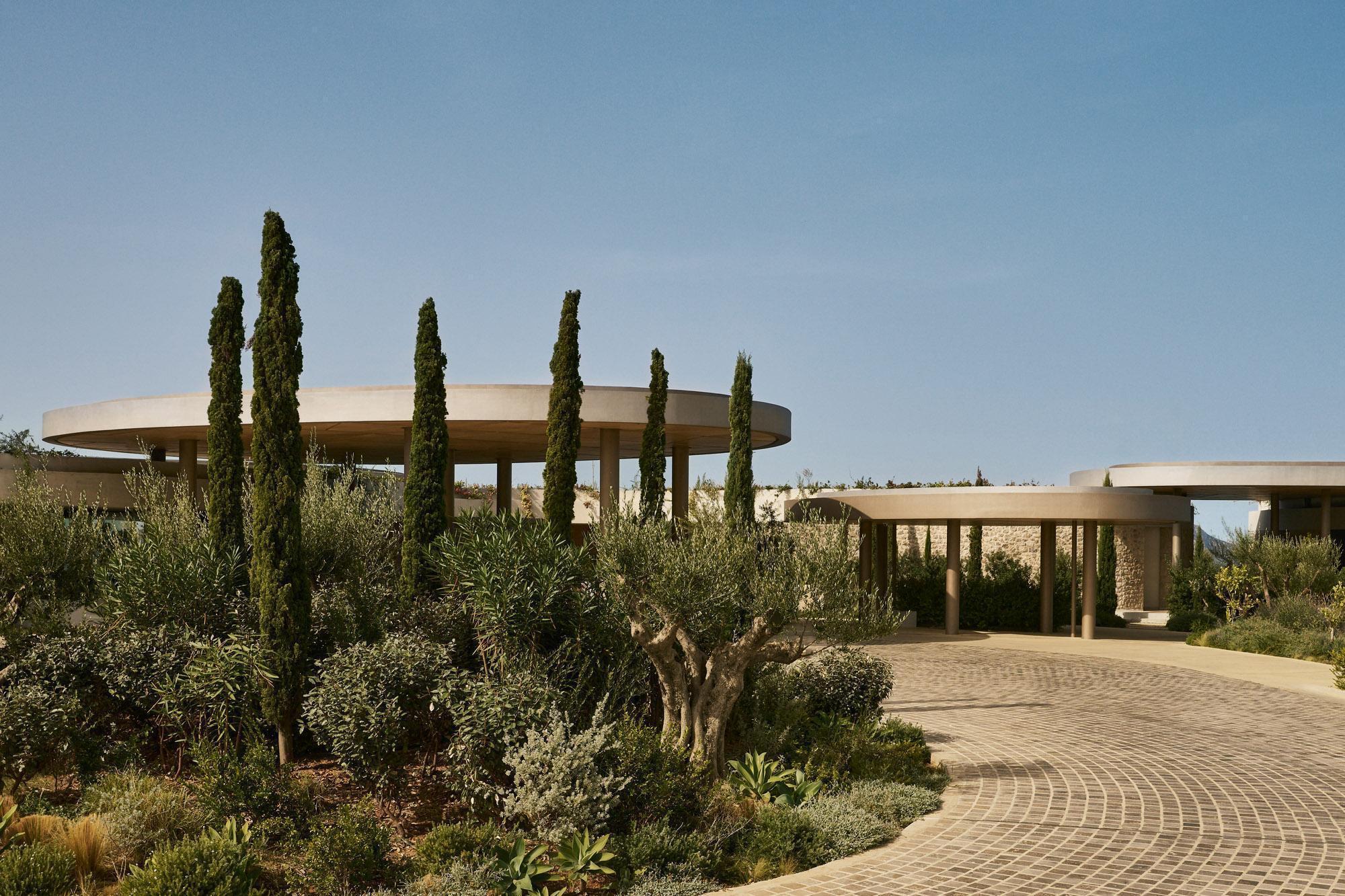 Curved canopy entrance with cylindrical columns framed by tall cypress trees and a paved driveway