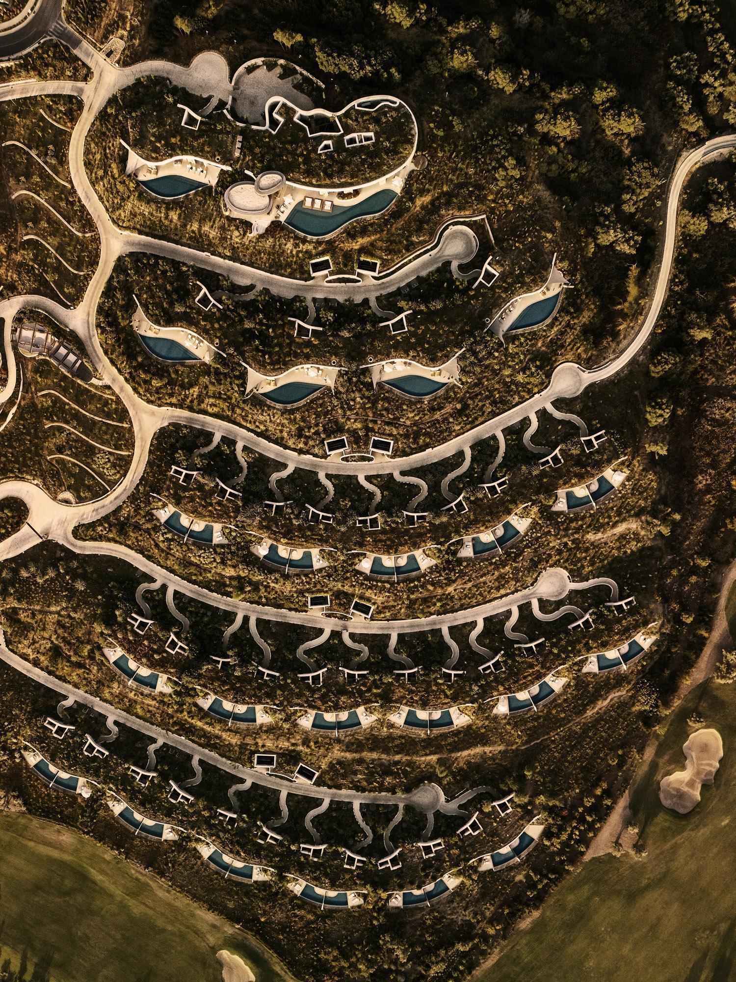 Aerial view of terraced hillside development with curved pathways and pools winding through dense vegetation