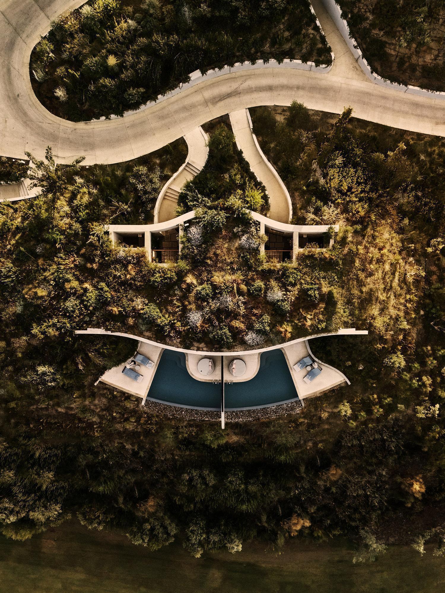 Drone view of crescent-shaped pool terrace flanked by two pavilions and curved winding paths