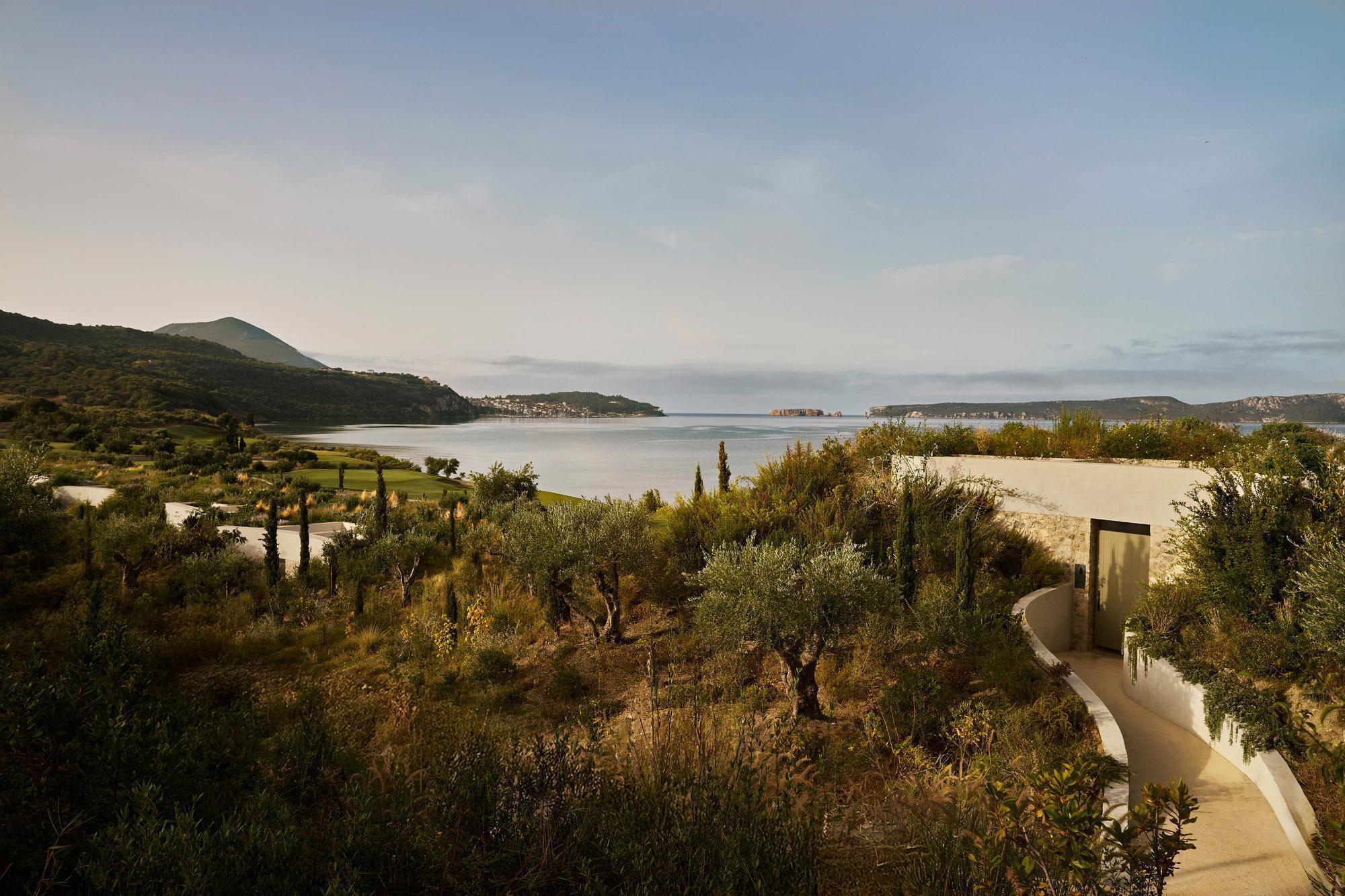 Curved roofline nestled among olive trees and cypress with coastal hills in the distance