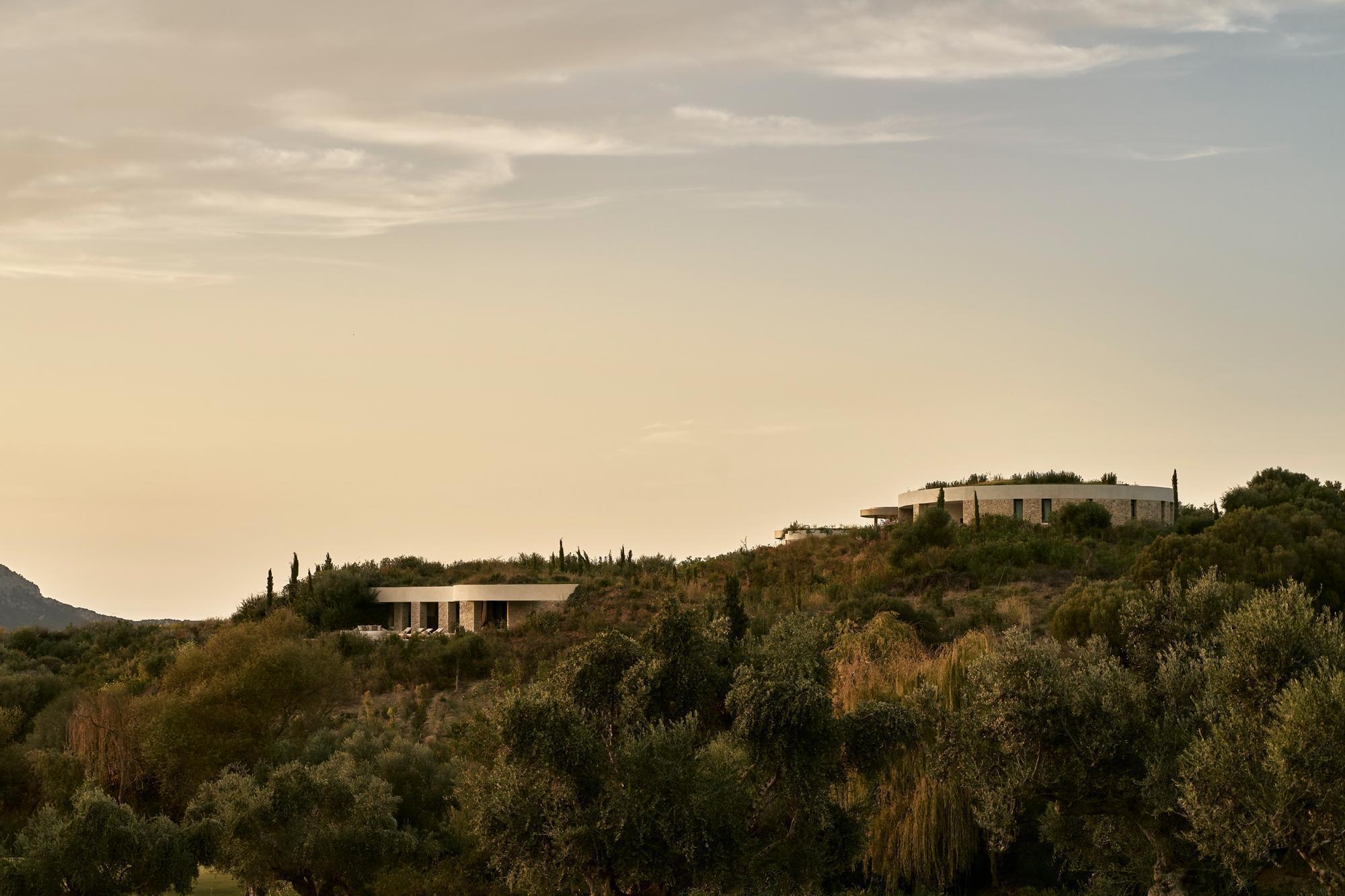Distant view of two low structures with flat roofs on a hillside at dusk