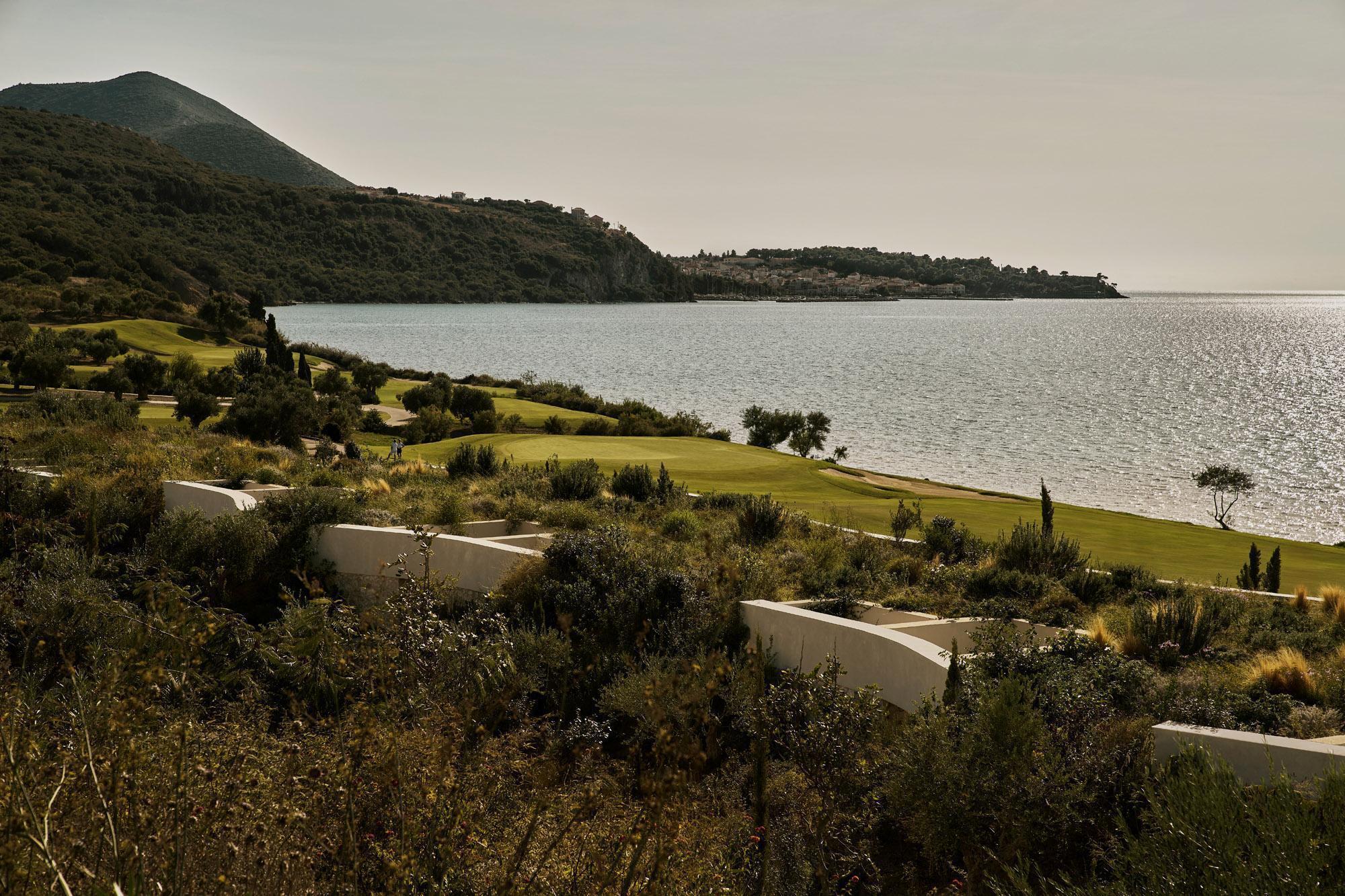 White concrete retaining walls terracing down the sloping landscape toward the sea and mountains