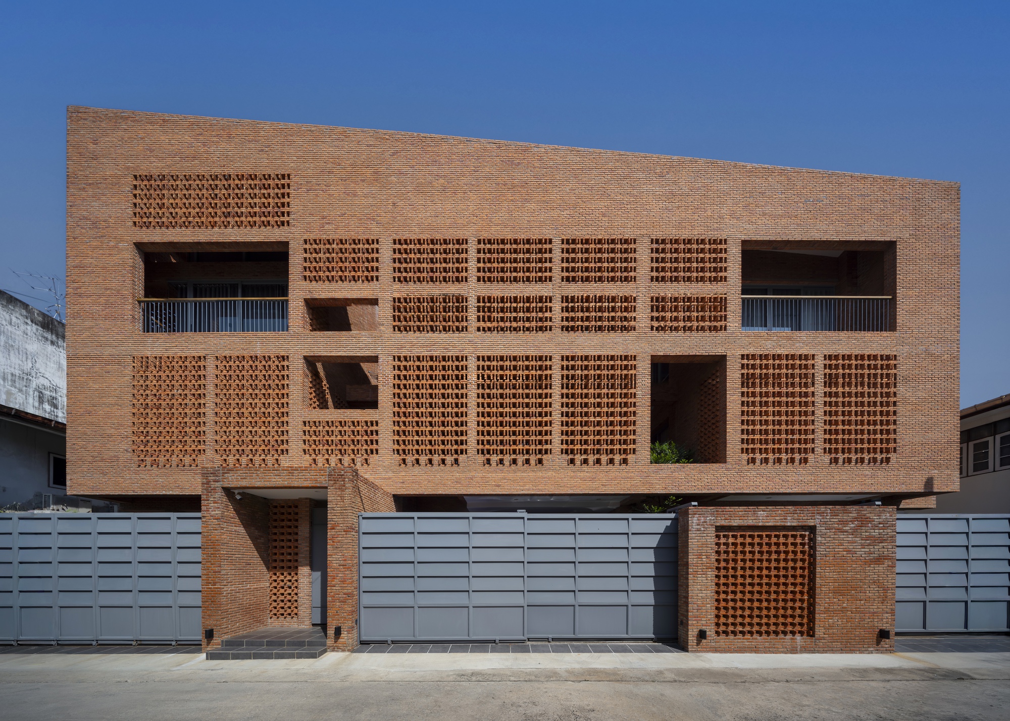 Street facade with patterned brickwork screens and grey metal gates under a clear blue sky