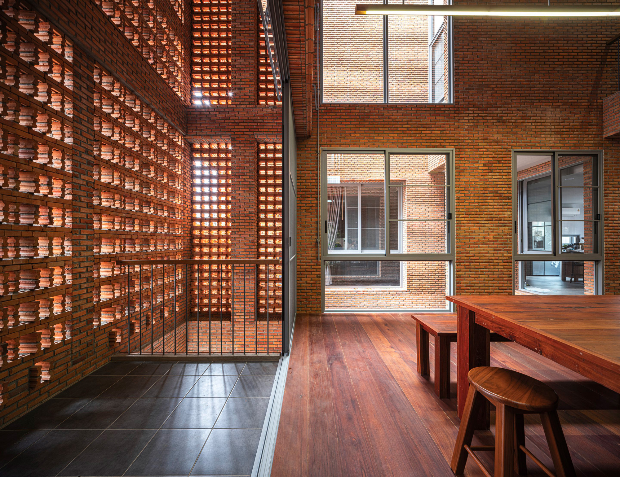 Interior terrace with timber furniture alongside backlit perforated brick screen wall at dusk