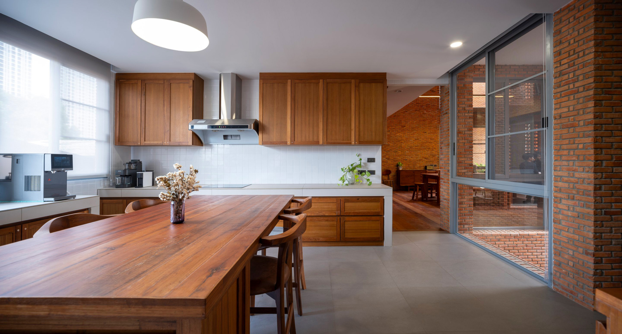 Kitchen with timber cabinetry and island opening to a brick courtyard through full-height glazing