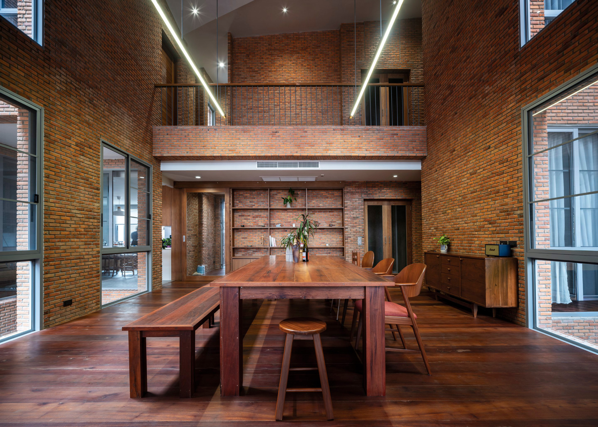 Double-height dining space with exposed brick walls and a timber mezzanine bridge above