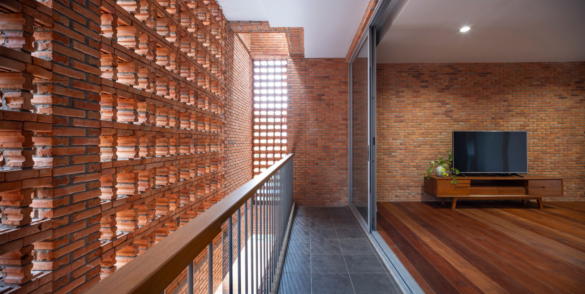 Upper corridor with perforated brick screen wall filtering daylight along the timber floor