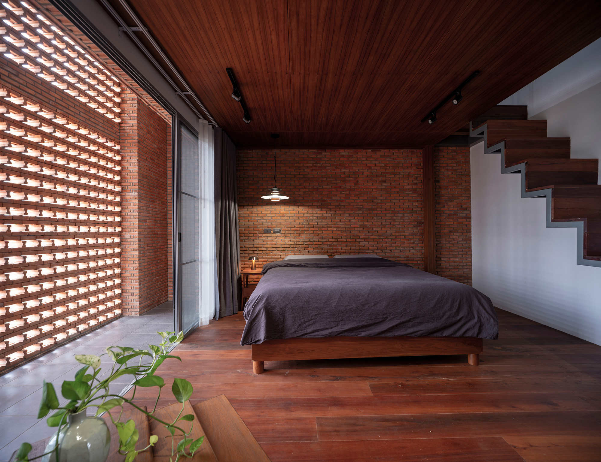 Bedroom with timber slat ceiling and perforated brick wall admitting dappled light