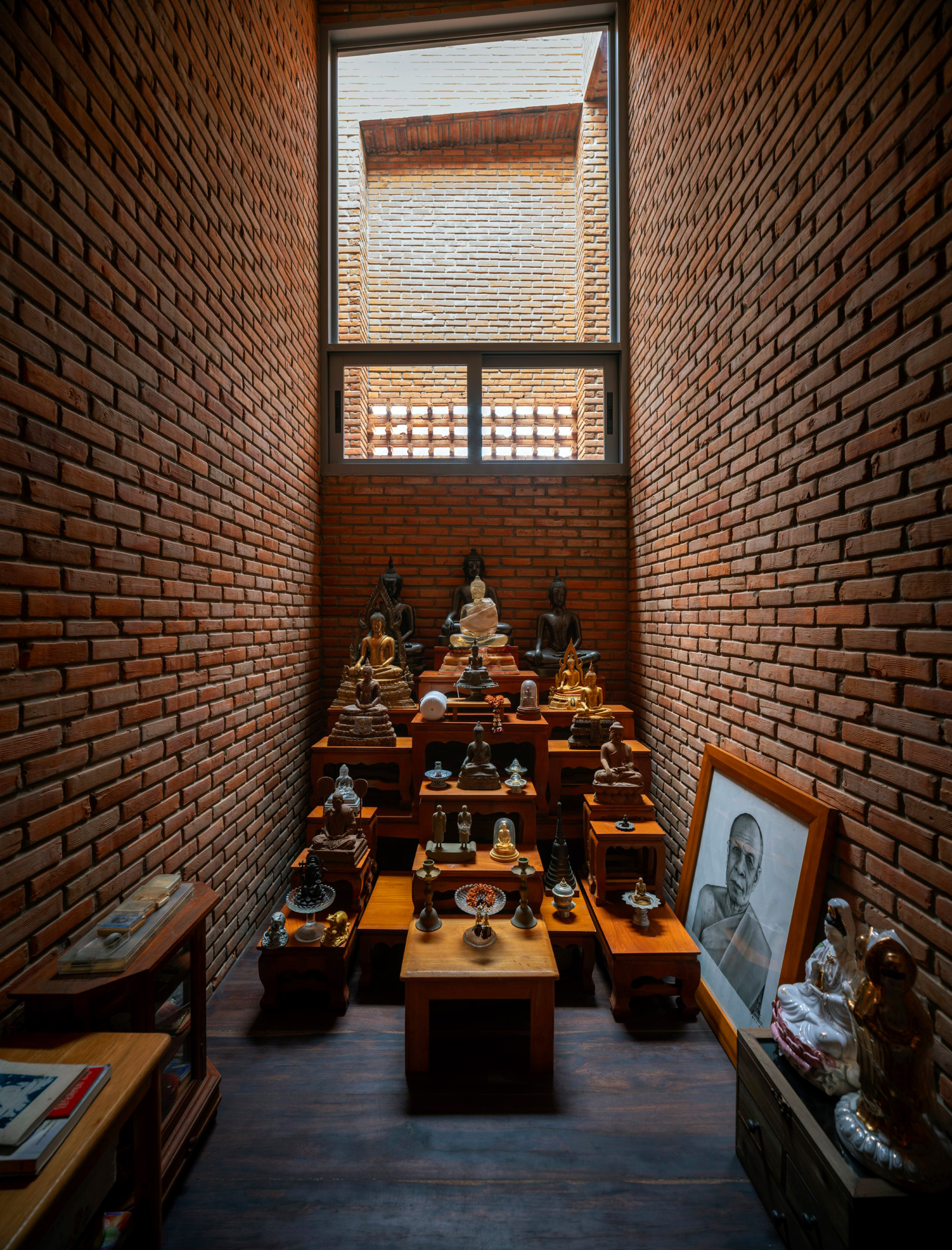 Prayer room with tiered timber shelves holding figurines beneath a tall clerestory window