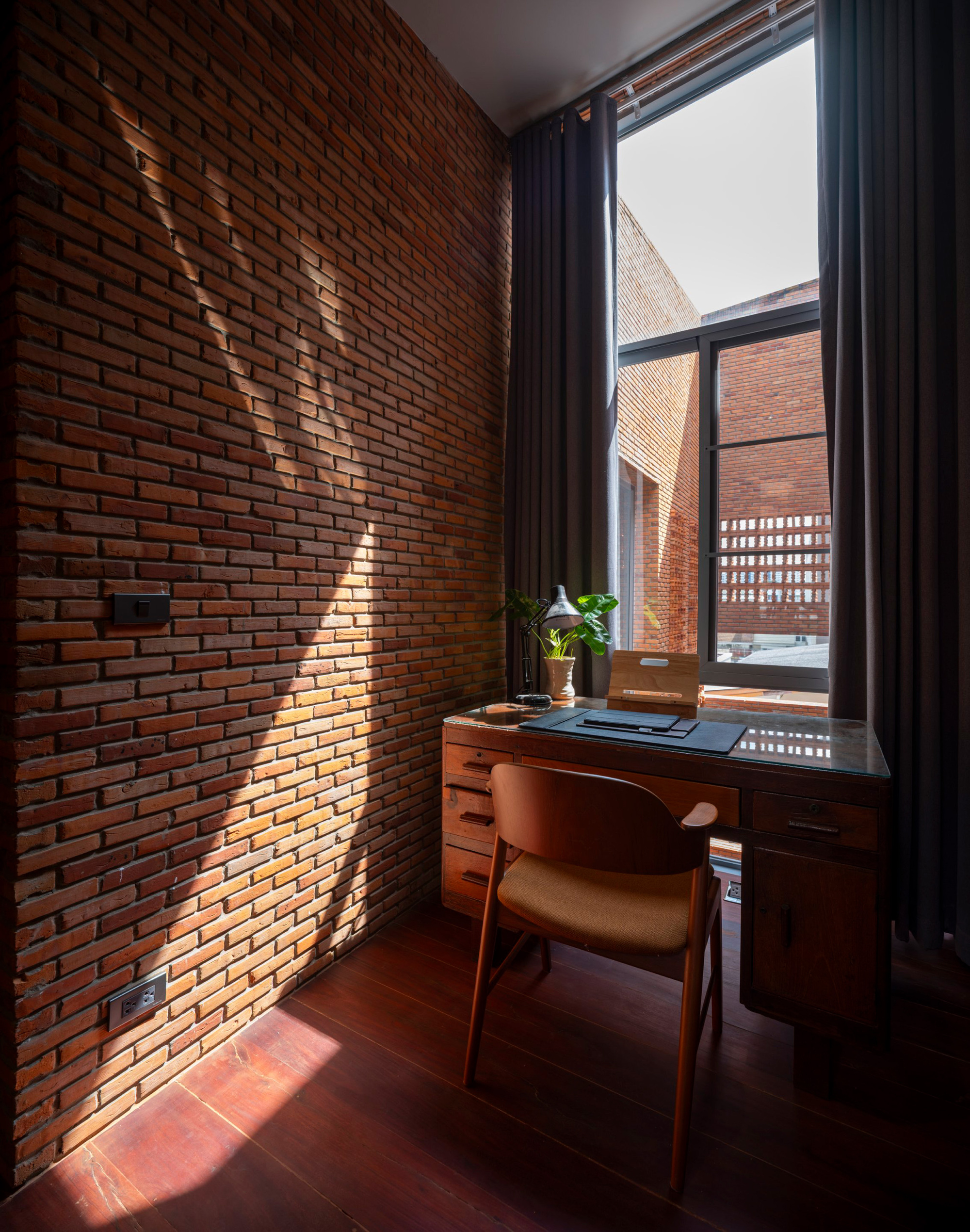Workspace with red brick wall and tall window framing a view of a perforated brick courtyard