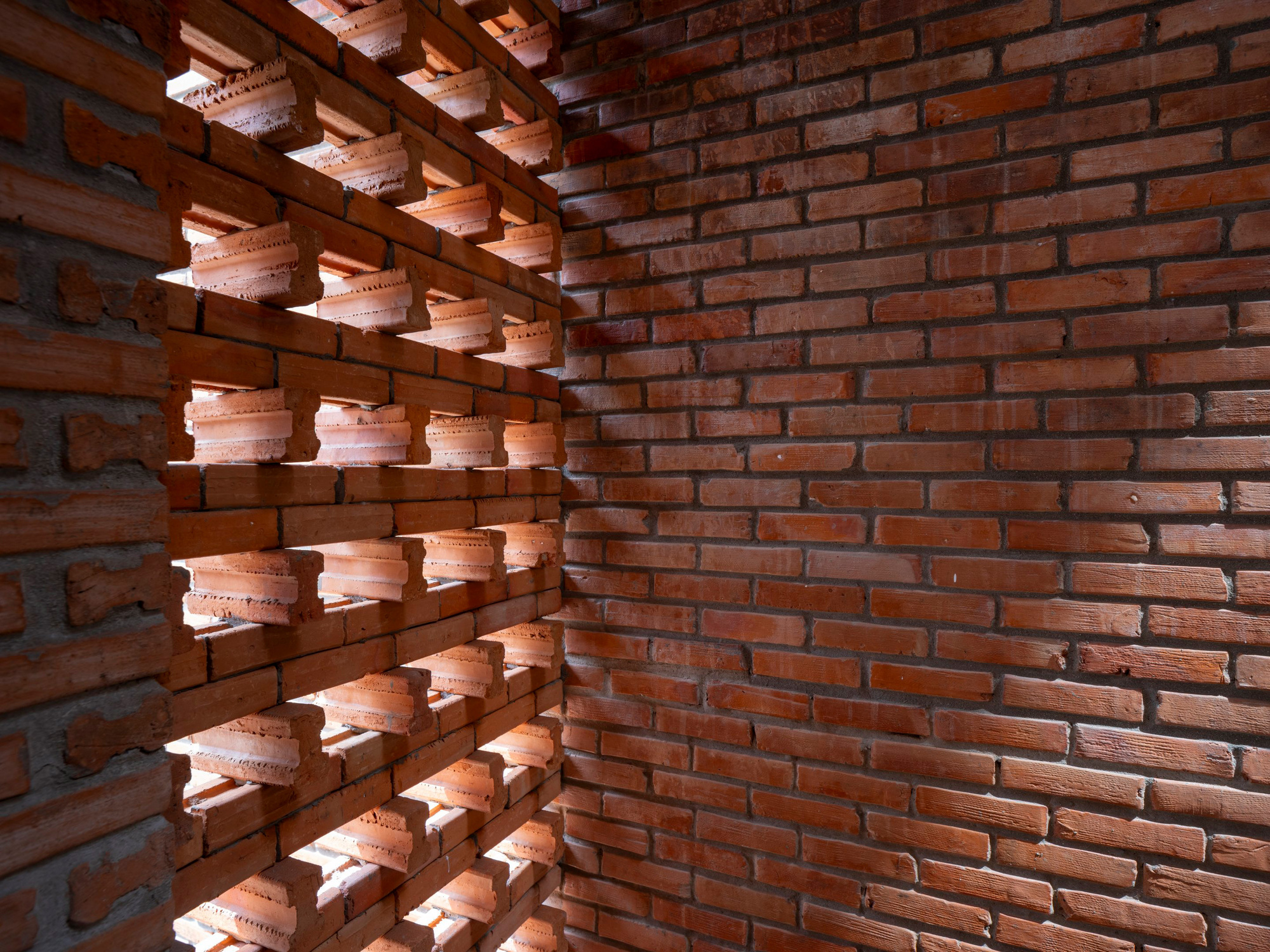 Corner detail where perforated brick screen meets solid brick wall with exposed timber joists above