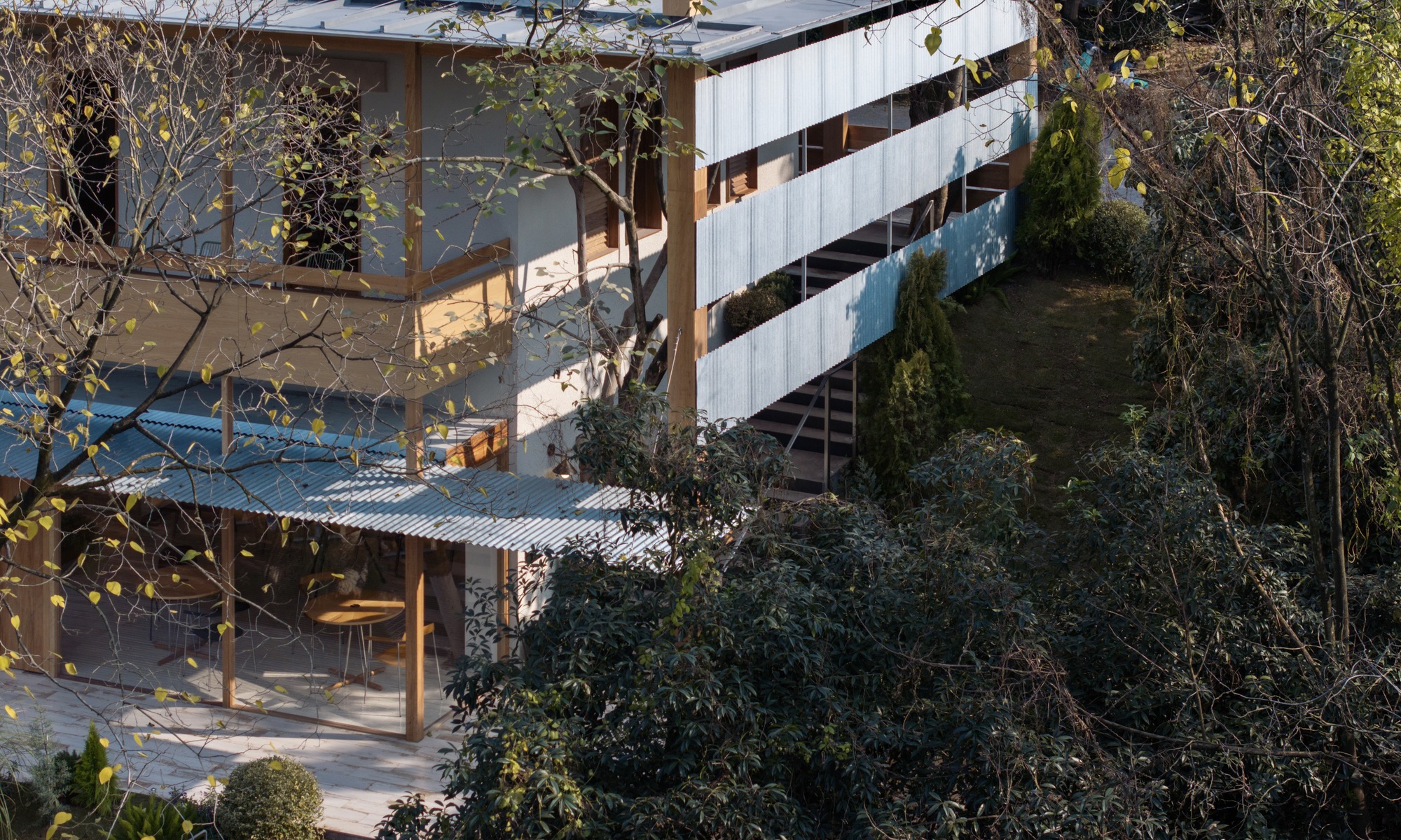 Elevated view of tiered terraces with corrugated metal roofs nestled into a sloped garden with bare trees
