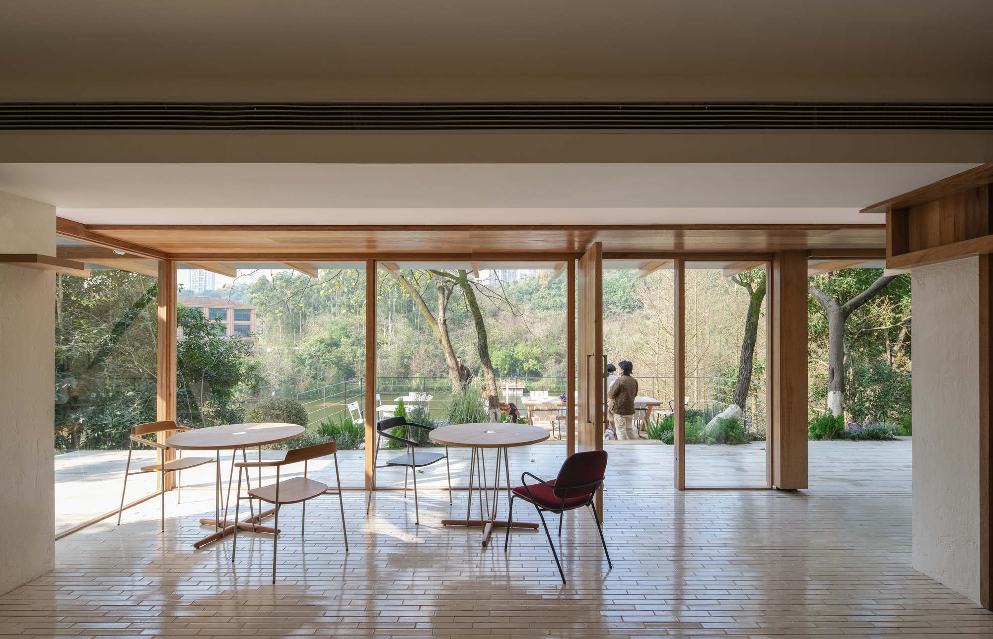 Interior dining area with timber-framed glazing opening to a garden terrace beneath a white ceiling
